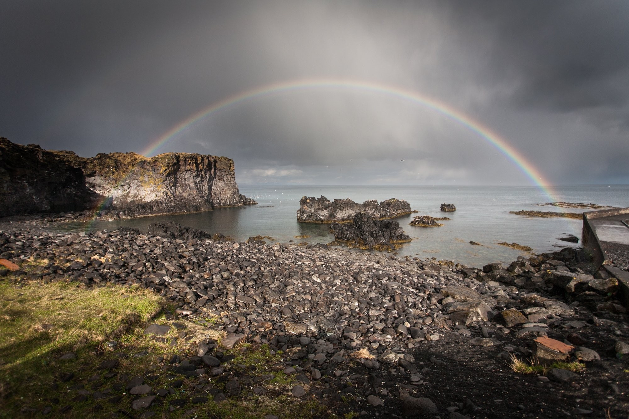 Foto do arco-íris completo sobre rochas e água