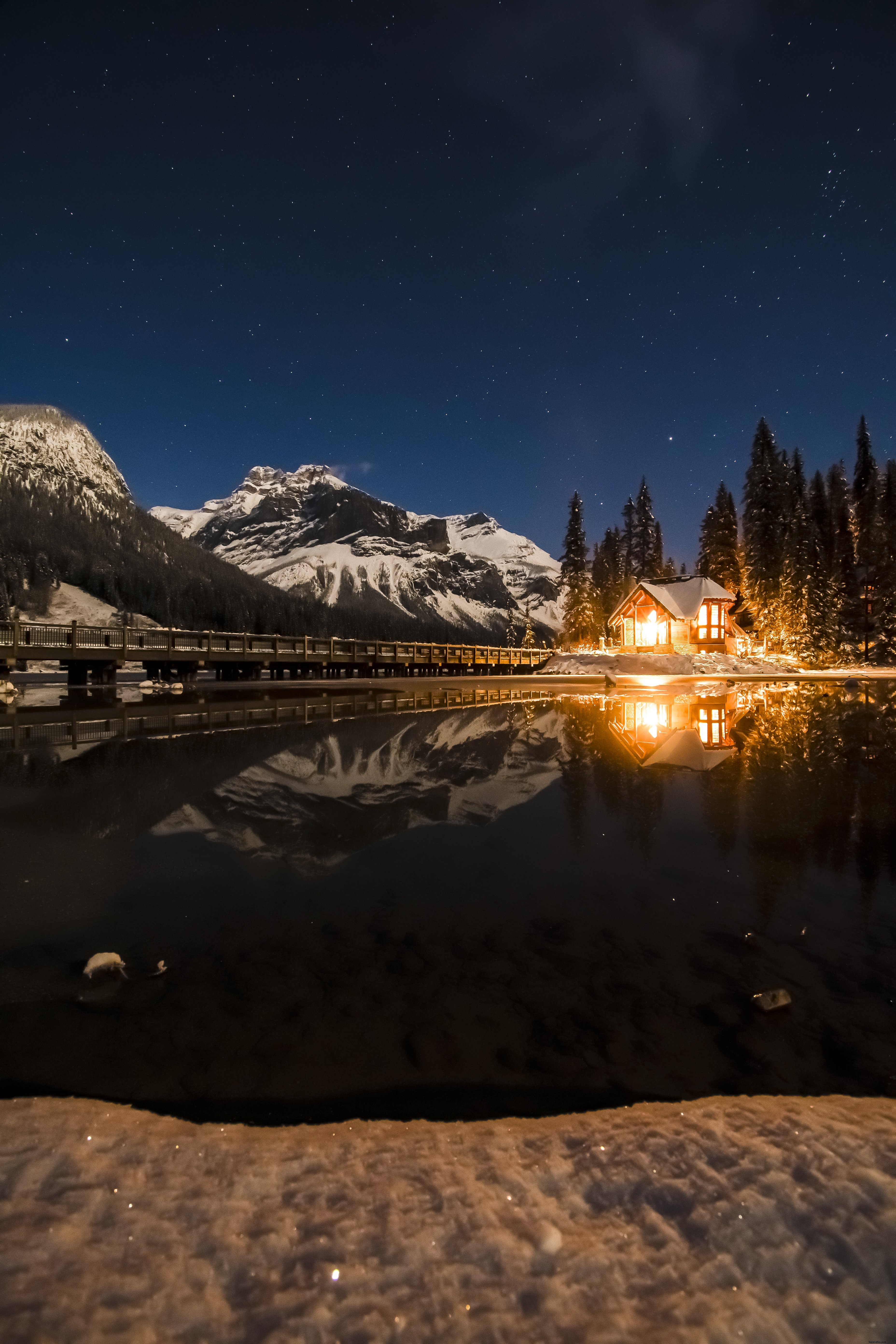 Casa iluminada por el fuego brilla junto a un lago helado contra un cielo estrellado Foto