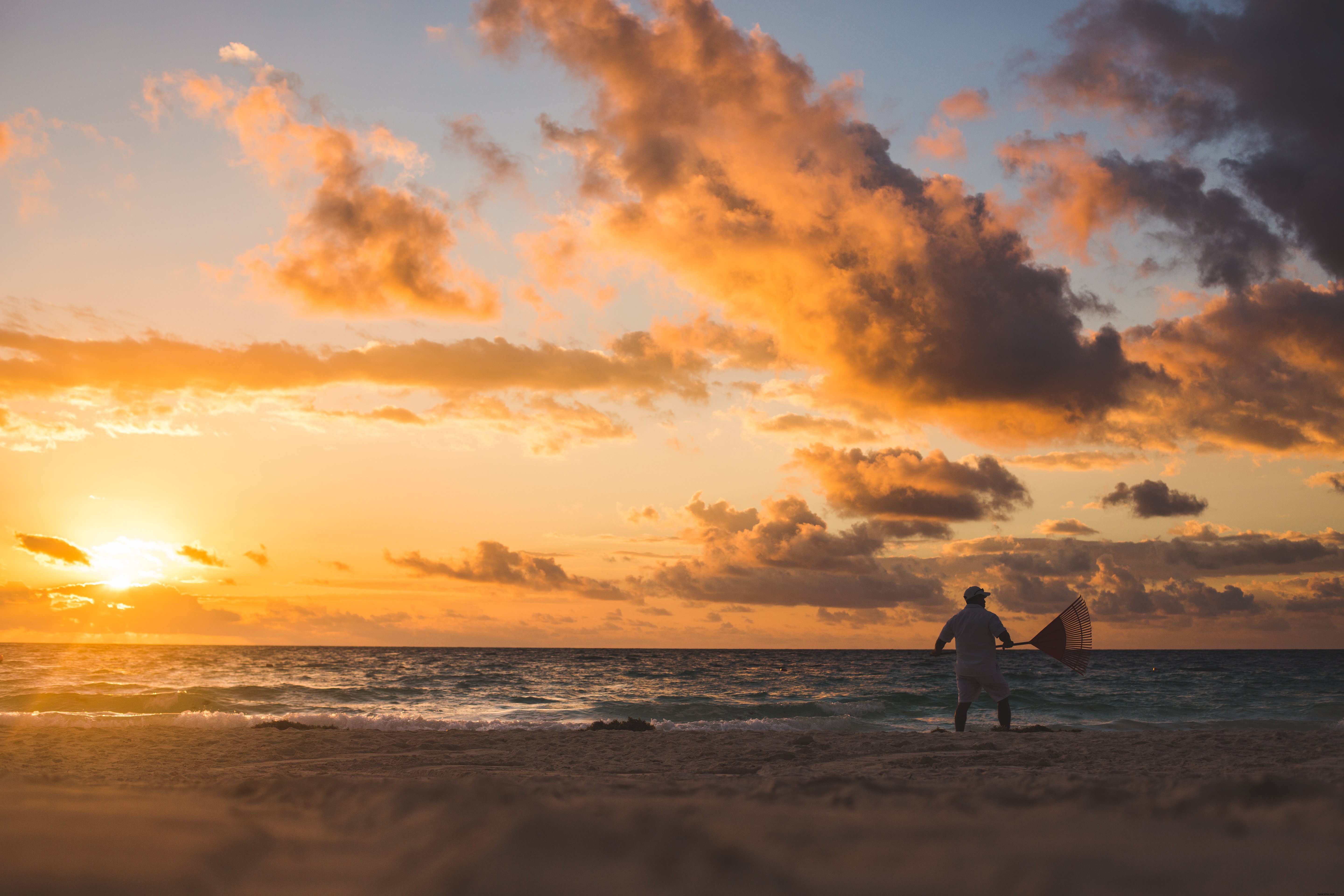 日没の写真でビーチを掻き集める男