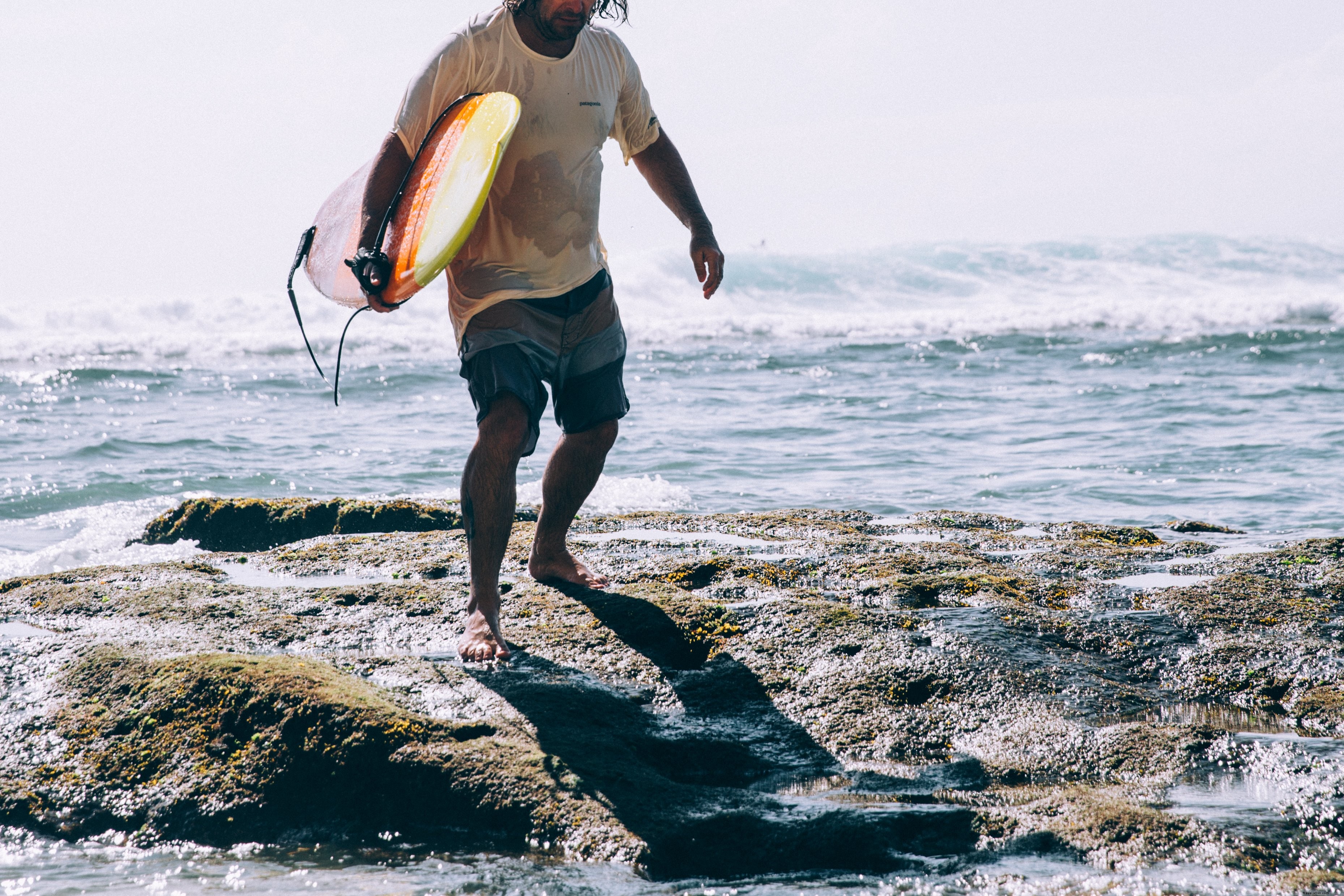 Hombre que lleva una tabla de surf emerge de las olas del océano Foto