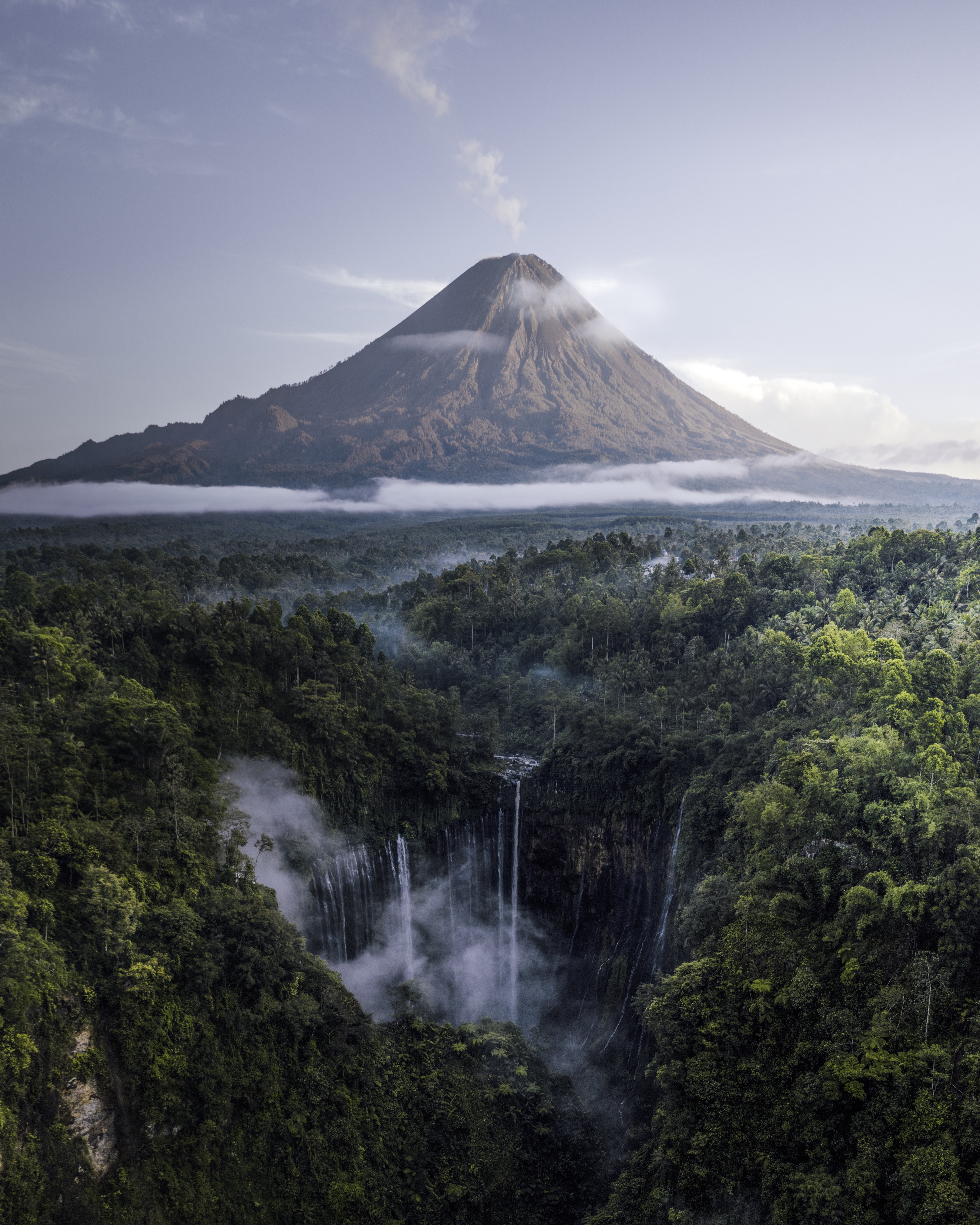 Cachoeiras na selva enquanto um vulcão fumega à distância Foto