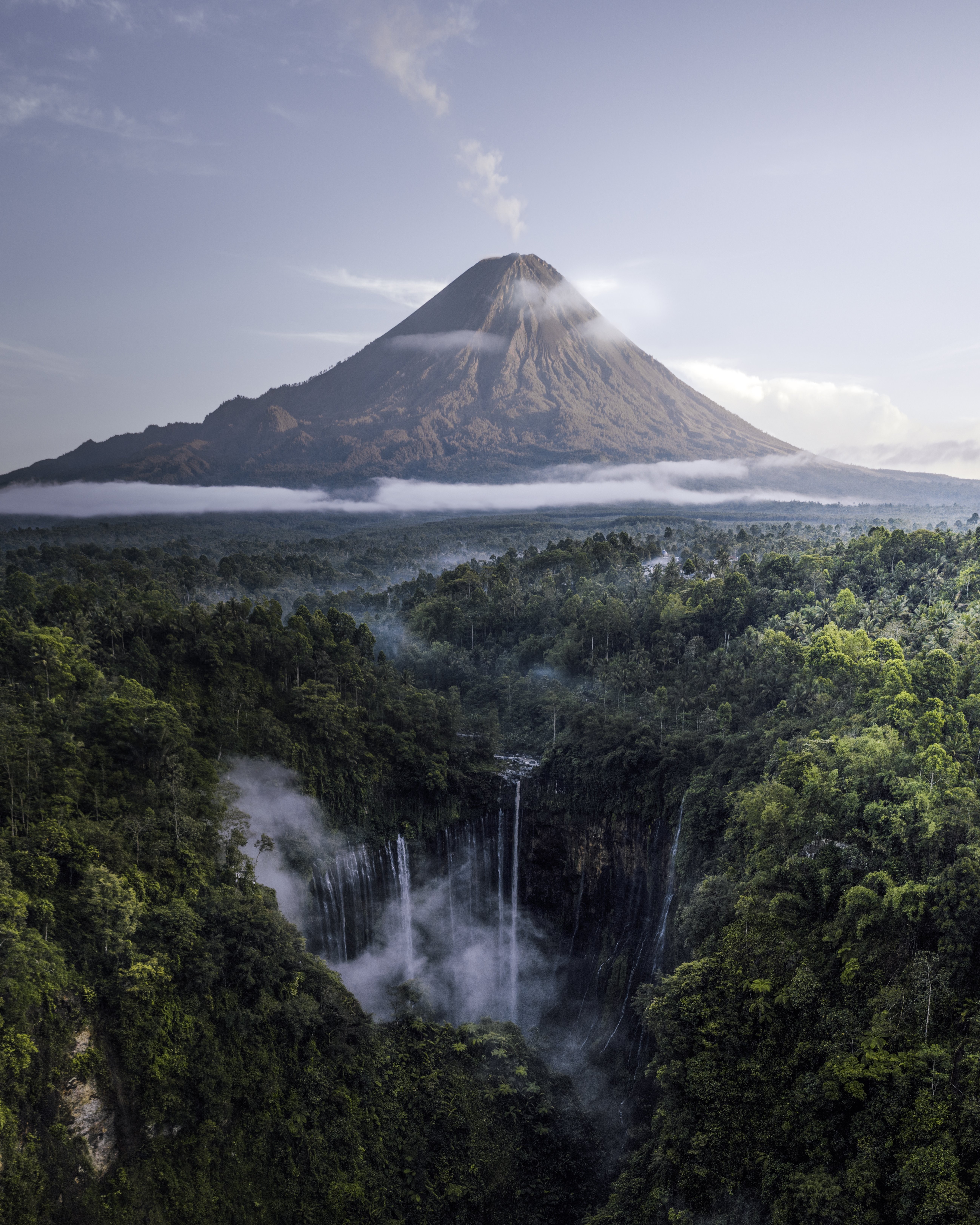 Air Terjun Di Hutan Saat Gunung Berapi Berasap Dari Kejauhan Foto