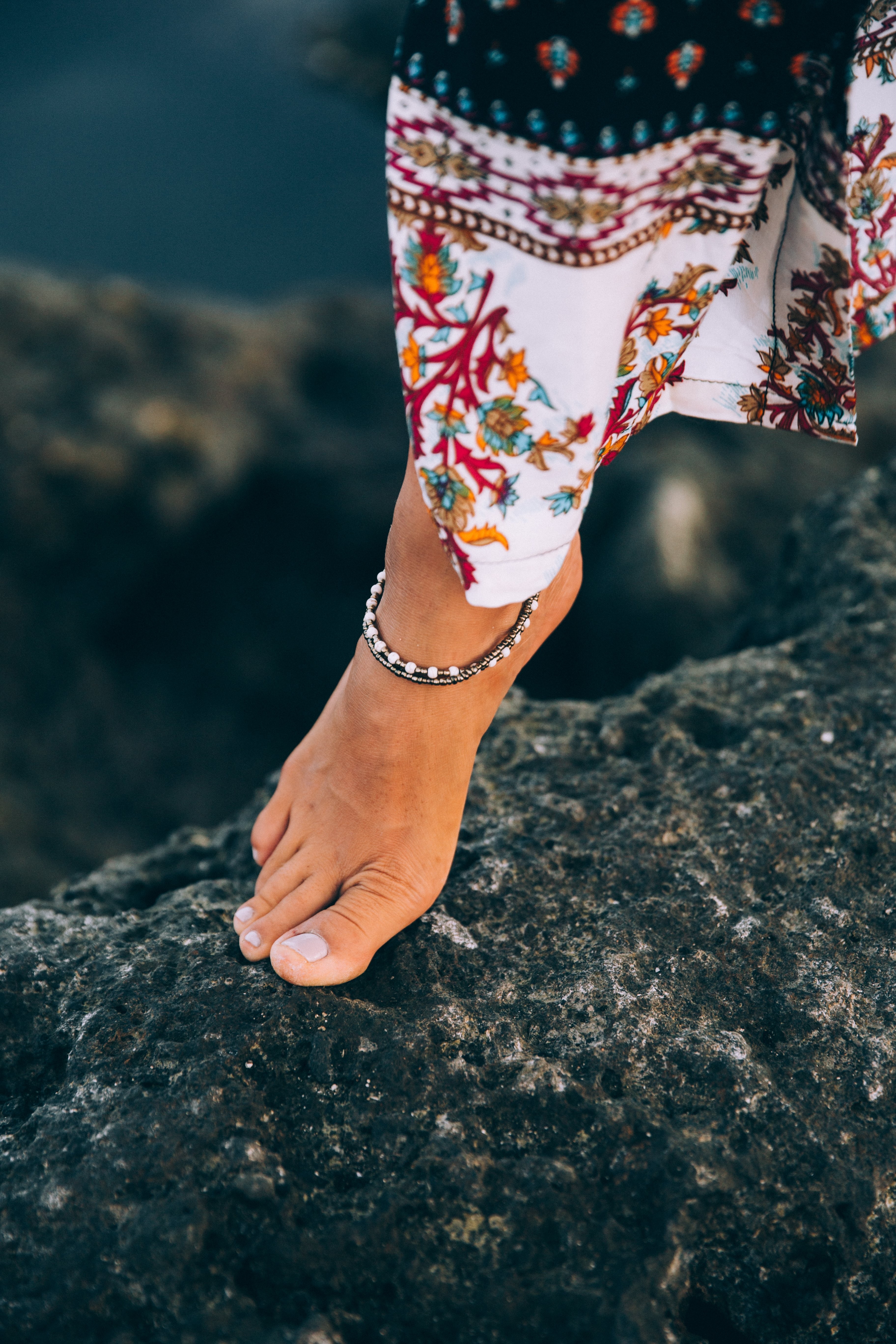 Uma mulher bronzeada exibe uma tornozeleira na foto do litoral rochoso
