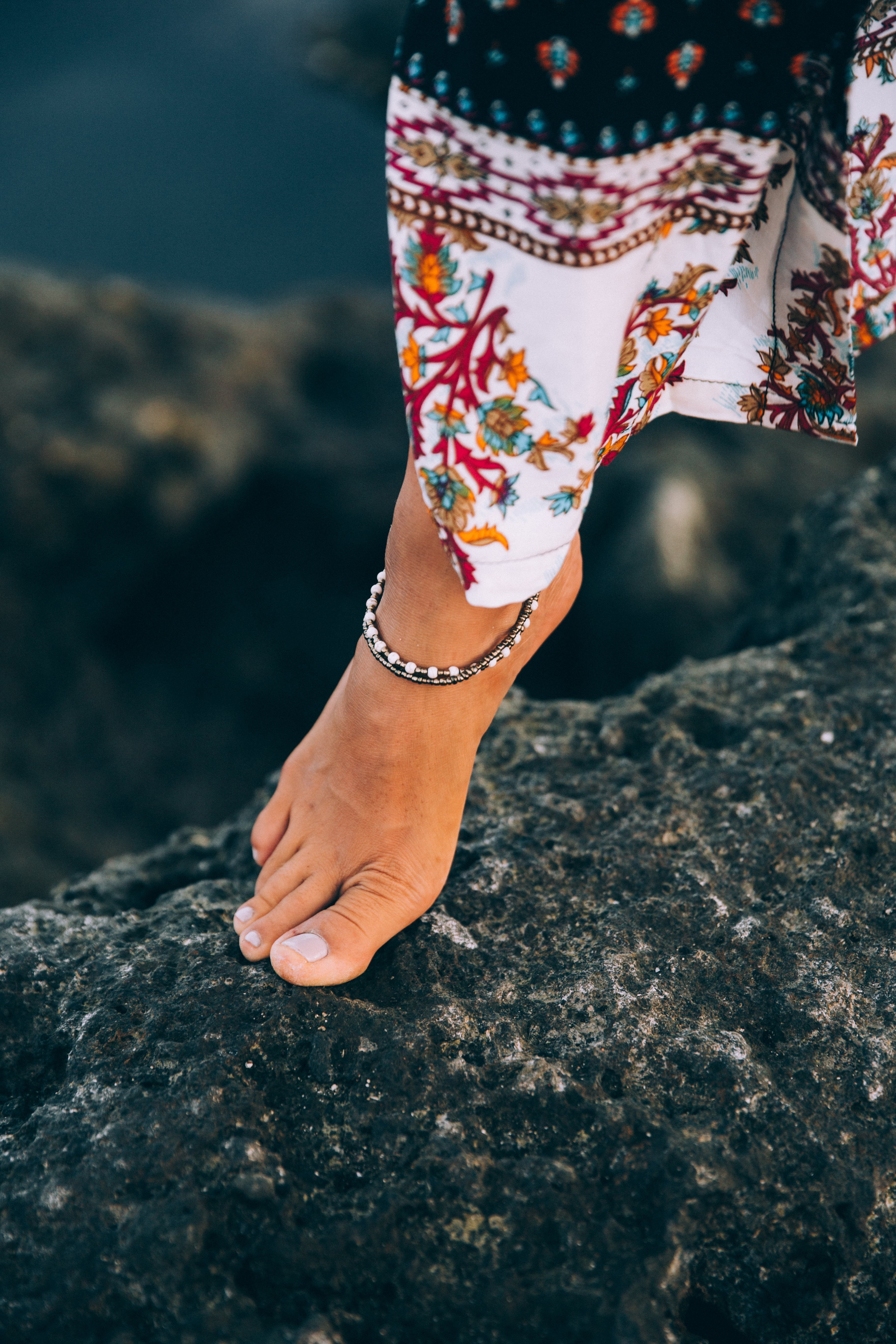 Seorang Wanita Kecokelatan Memamerkan Gelang Kaki Di Foto Pantai Berbatu