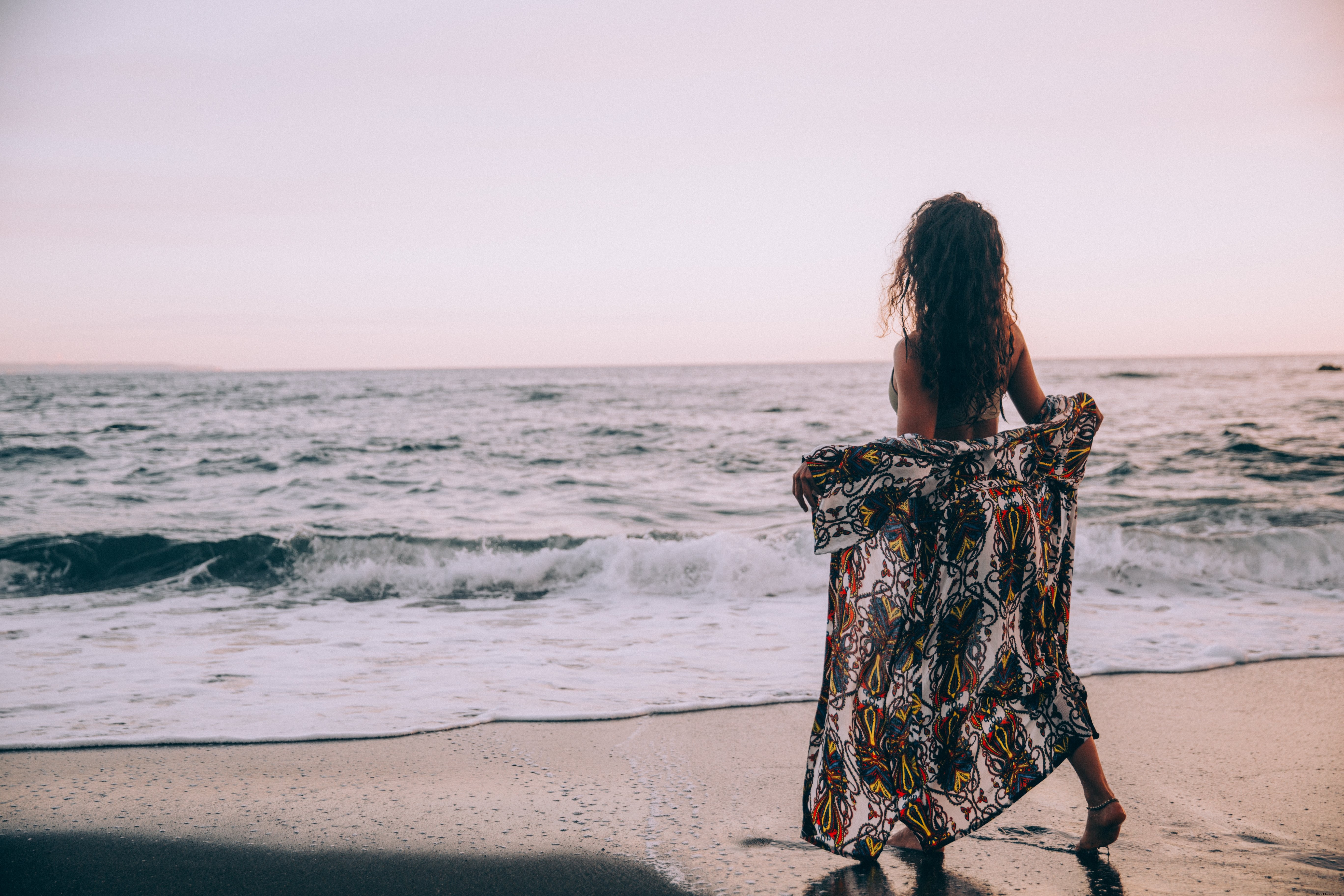 Une femme sur une plage ouvre son paréo à la photo des vagues