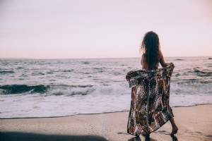 Une femme sur une plage ouvre son paréo à la photo des vagues