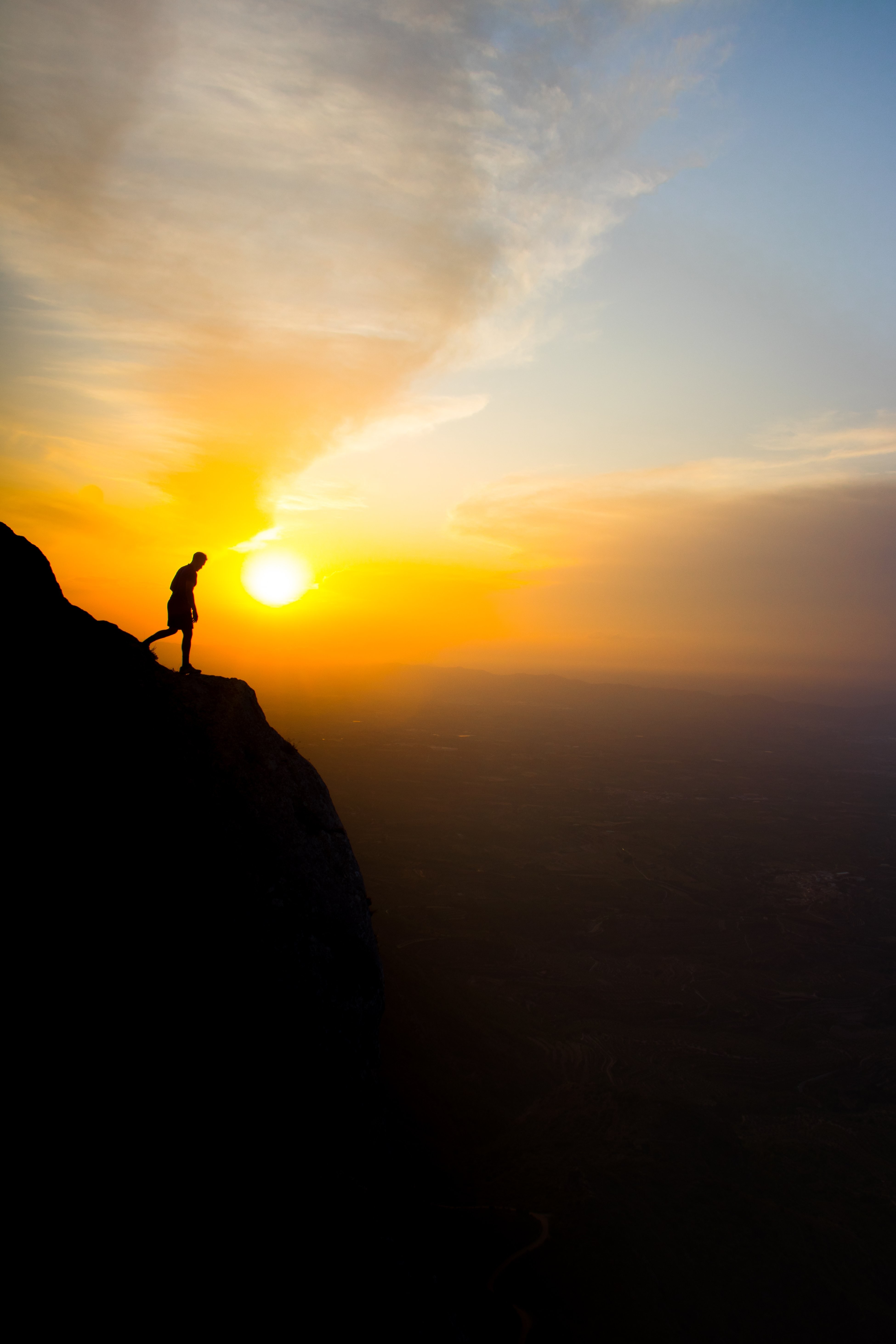 Silhueta de uma pessoa em pé em um penhasco ao pôr do sol. Foto