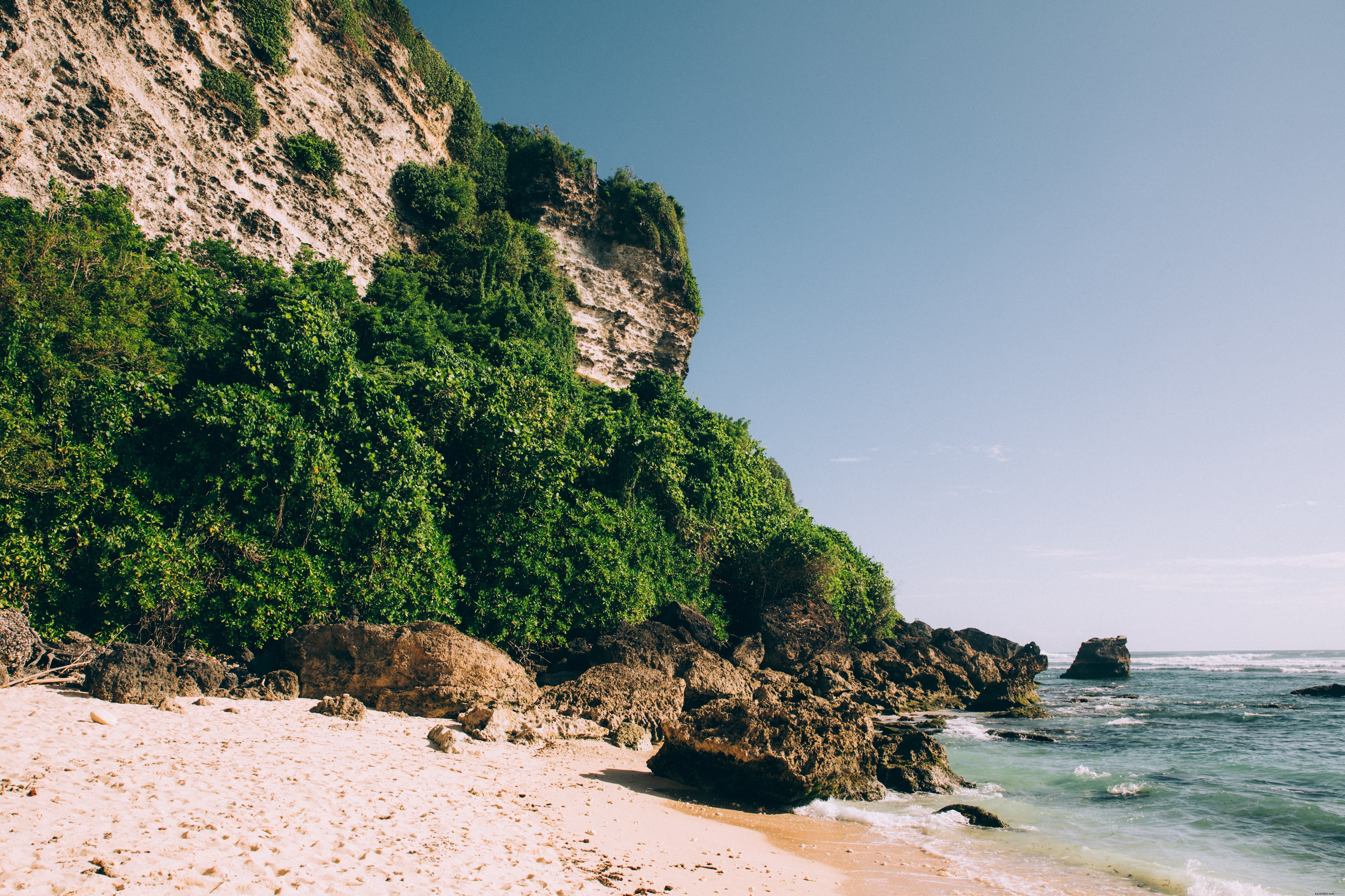 Spiaggia di sabbia circondata da scogliere rocciose e giungla foto