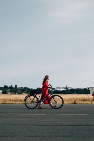 赤いドレスを着た人が自転車を道を歩く写真