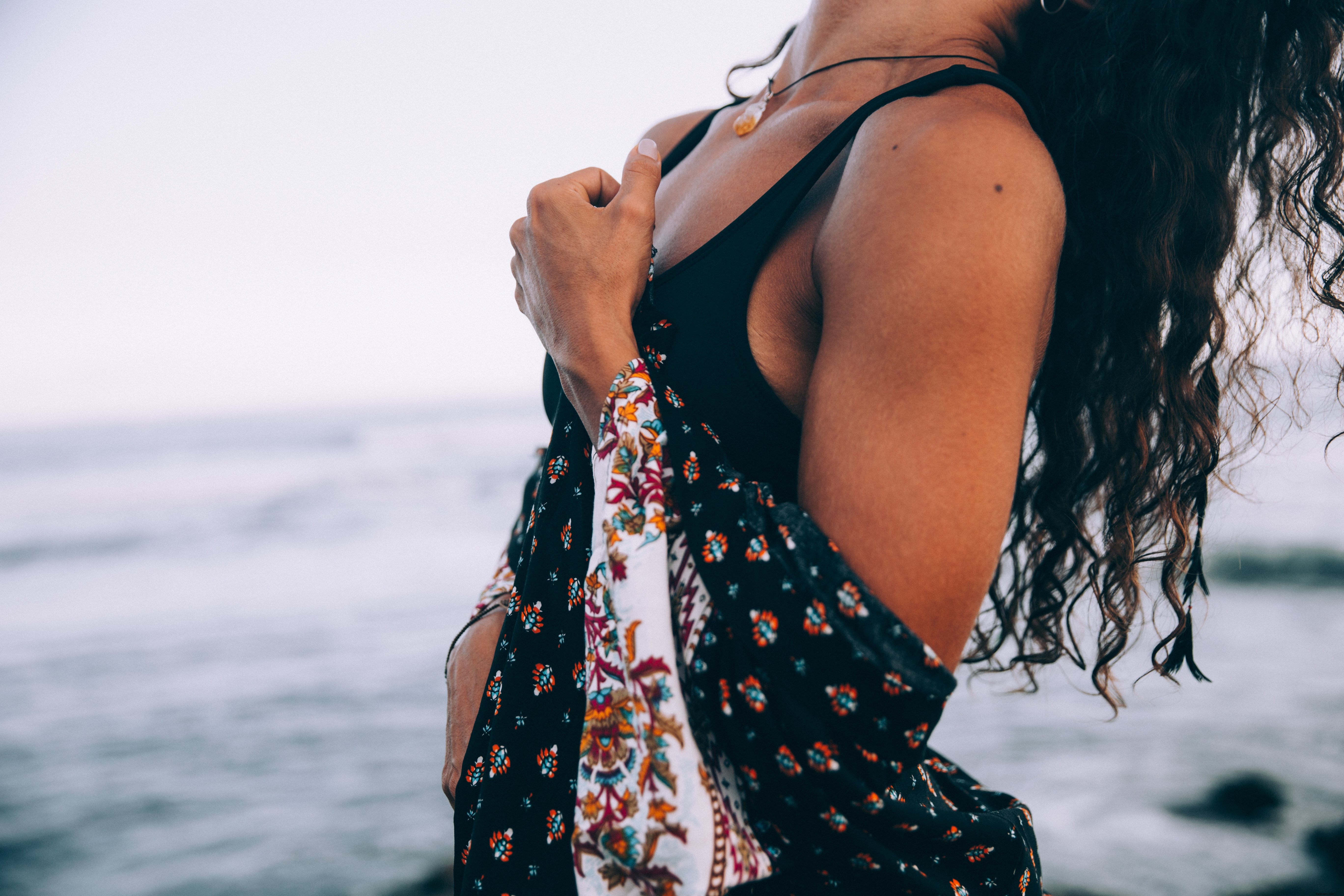 Uma mulher com manto estampado joga a cabeça para trás na foto da praia