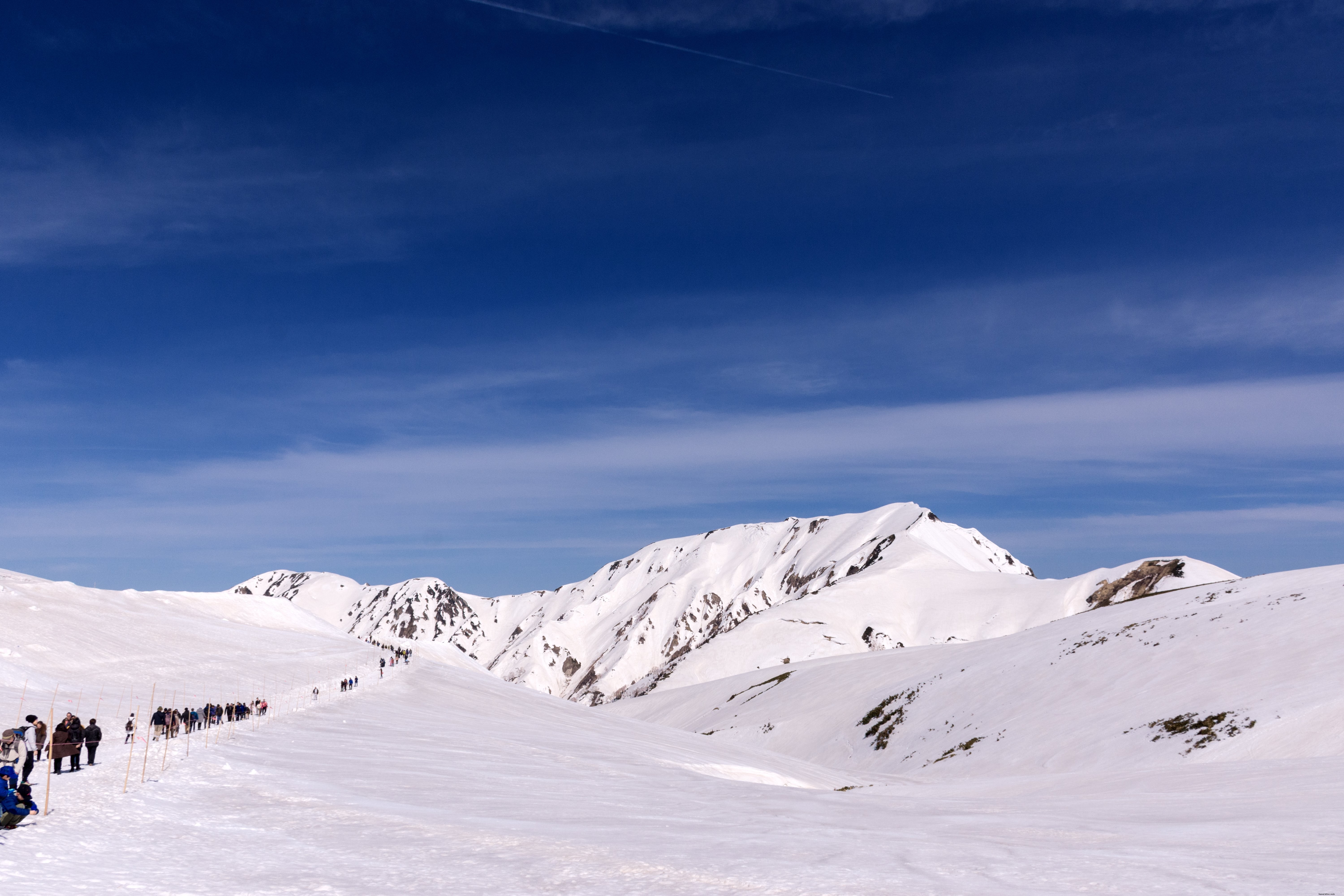 Una línea de excursionistas viaja a través de la foto de las montañas cubiertas de nieve