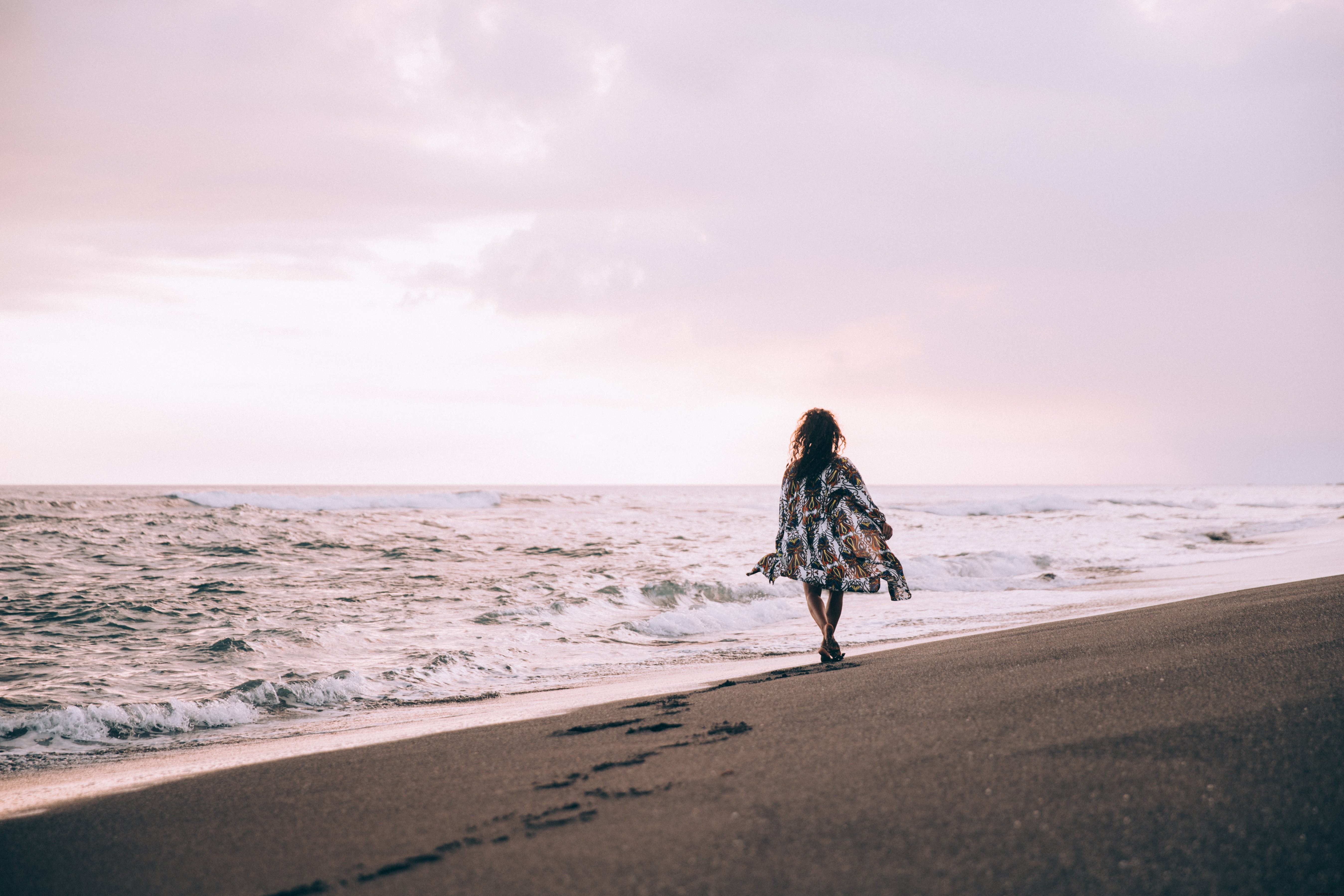 Uma mulher bronzeada em manto de praia esvoaçante caminha ao longo da praia Foto