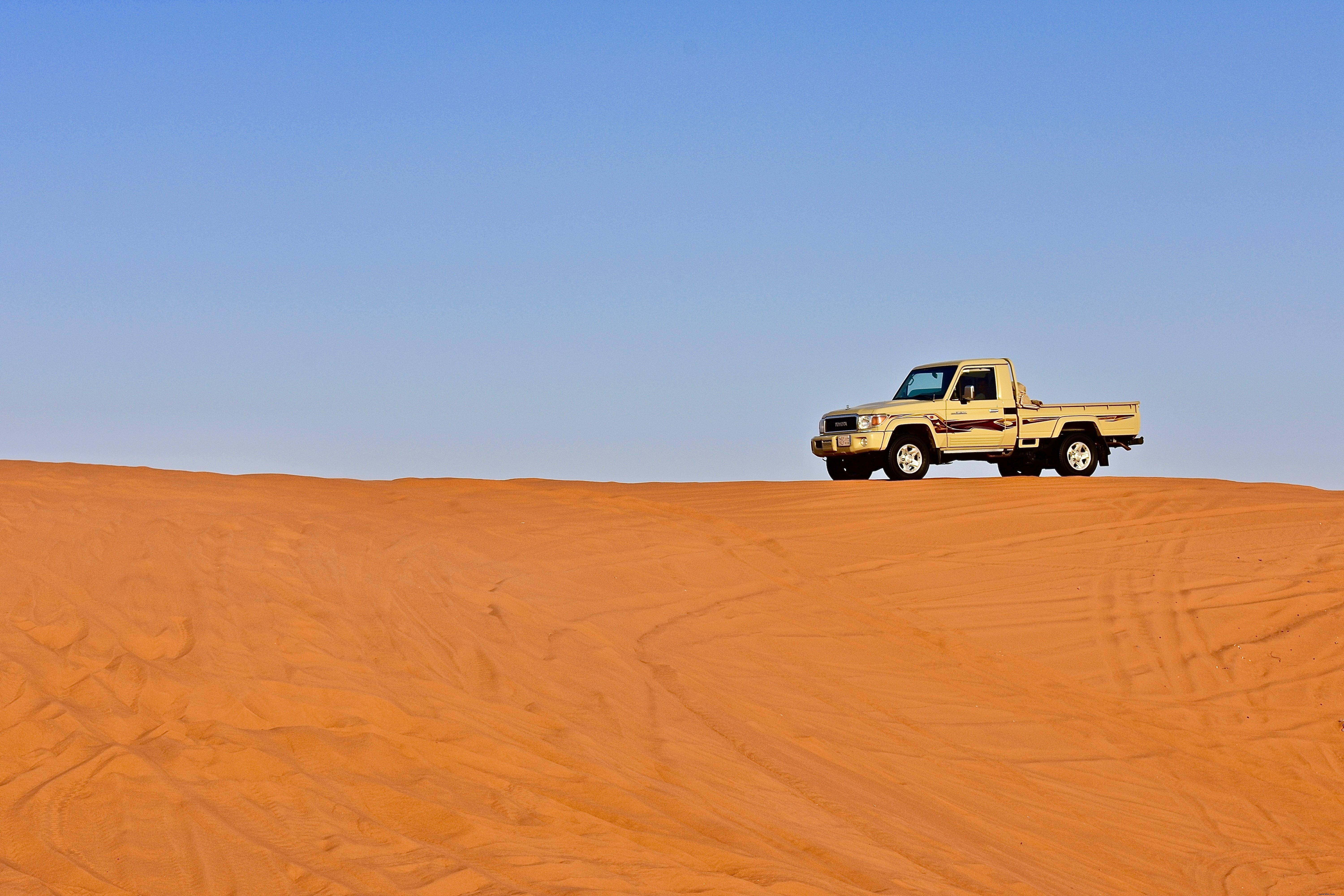 青い空の写真の下で砂漠の砂丘のピックアップトラック