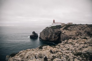 白塗りの灯台が岩だらけの崖の写真の上に立っている