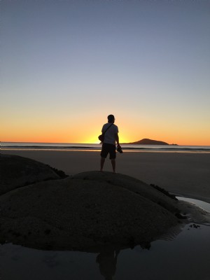 Um homem em uma duna observa o pôr do sol na praia.