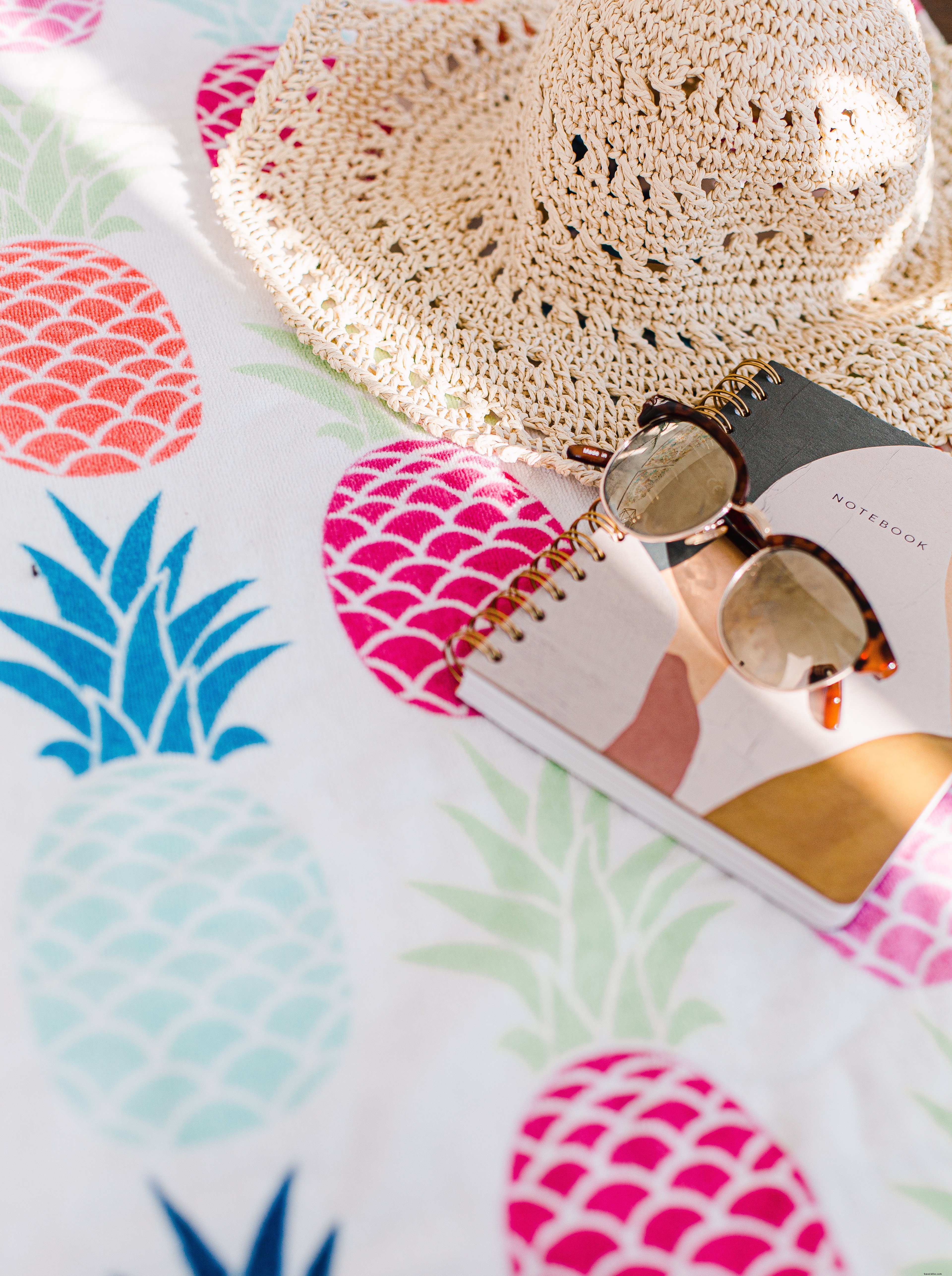 Cuaderno con gorro para el sol y gafas de sol sobre un mantel de piña Foto