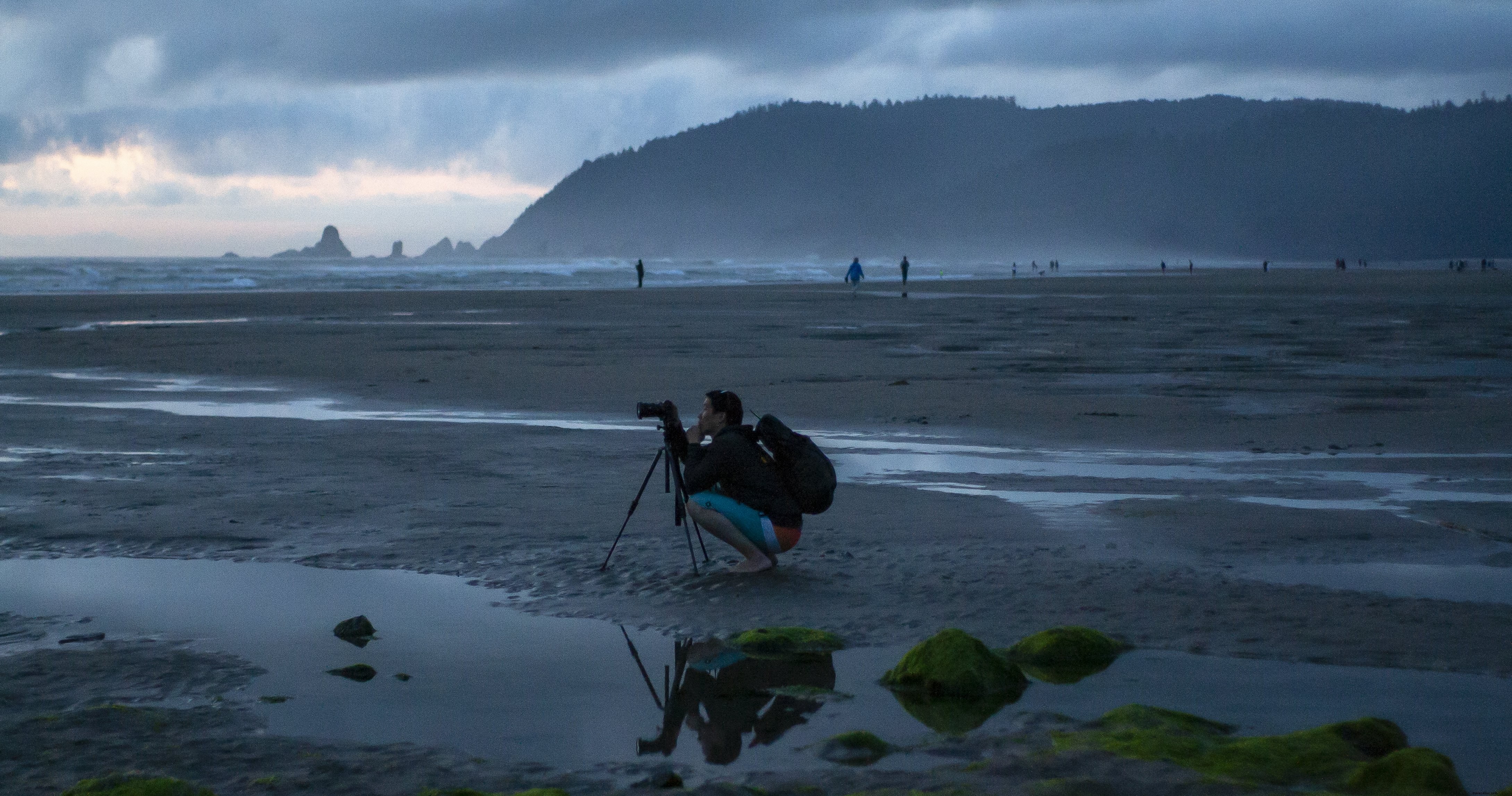 写真家が霧のビーチの写真で彼の三脚にしゃがむ
