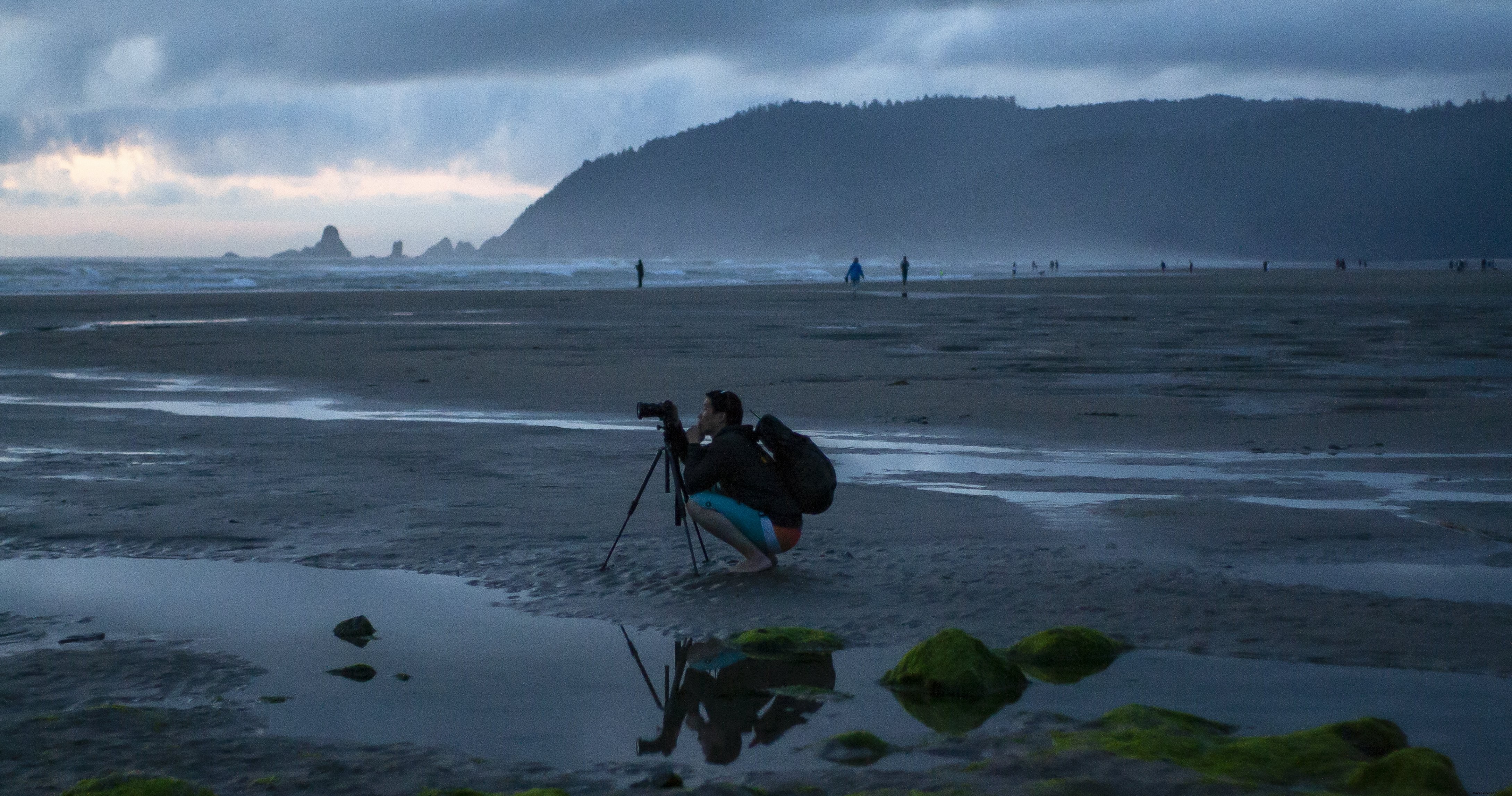 Um fotógrafo se agacha em seu tripé em uma foto de praia enevoada