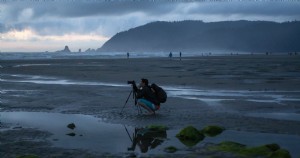 Um fotógrafo se agacha em seu tripé em uma foto de praia enevoada