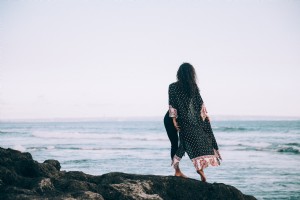 Uma mulher com um manto estampado esvoaçante está de pé ao lado da água. Foto