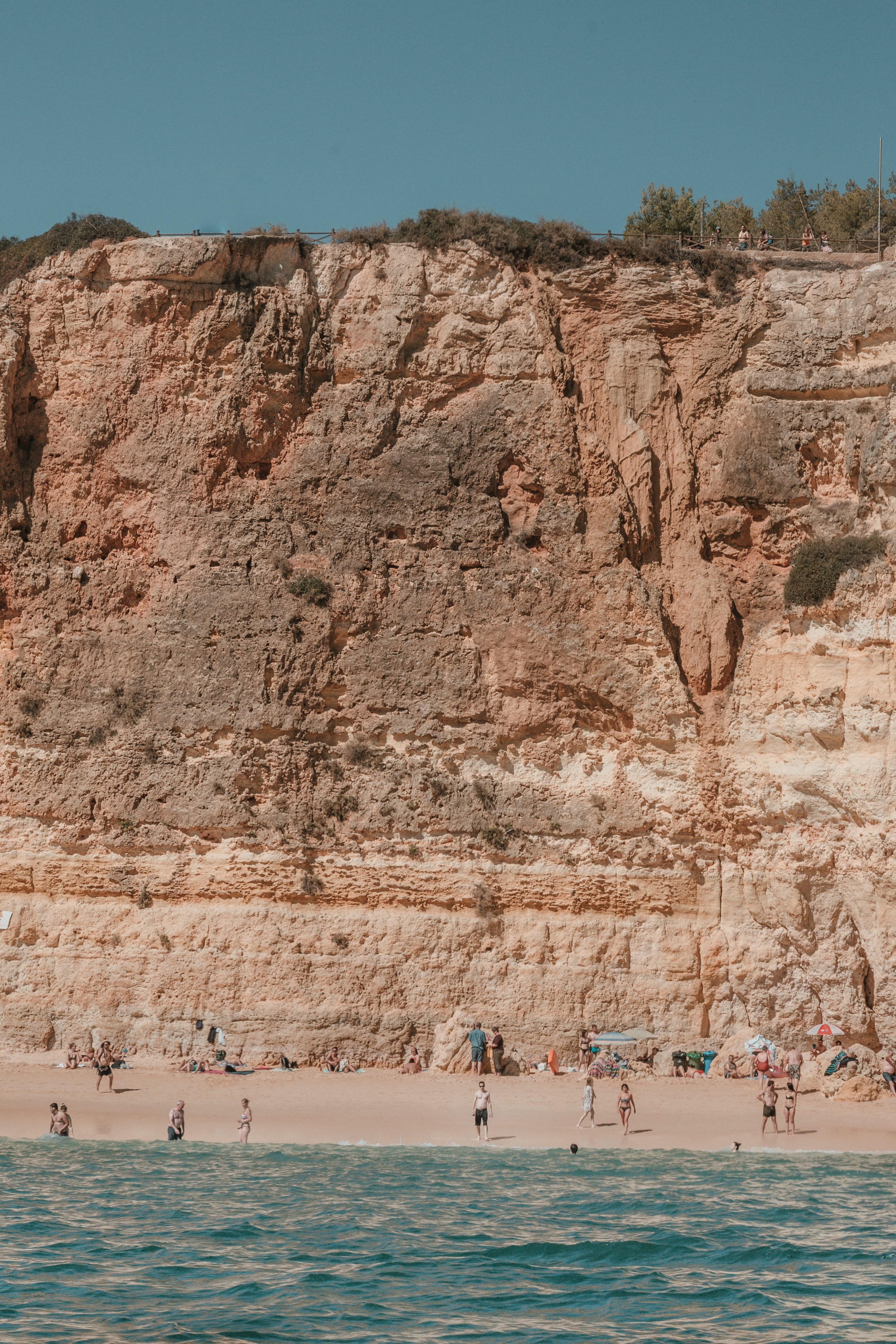 Penhascos rachados pelo sol com vista para banhistas em uma foto de uma praia de areia