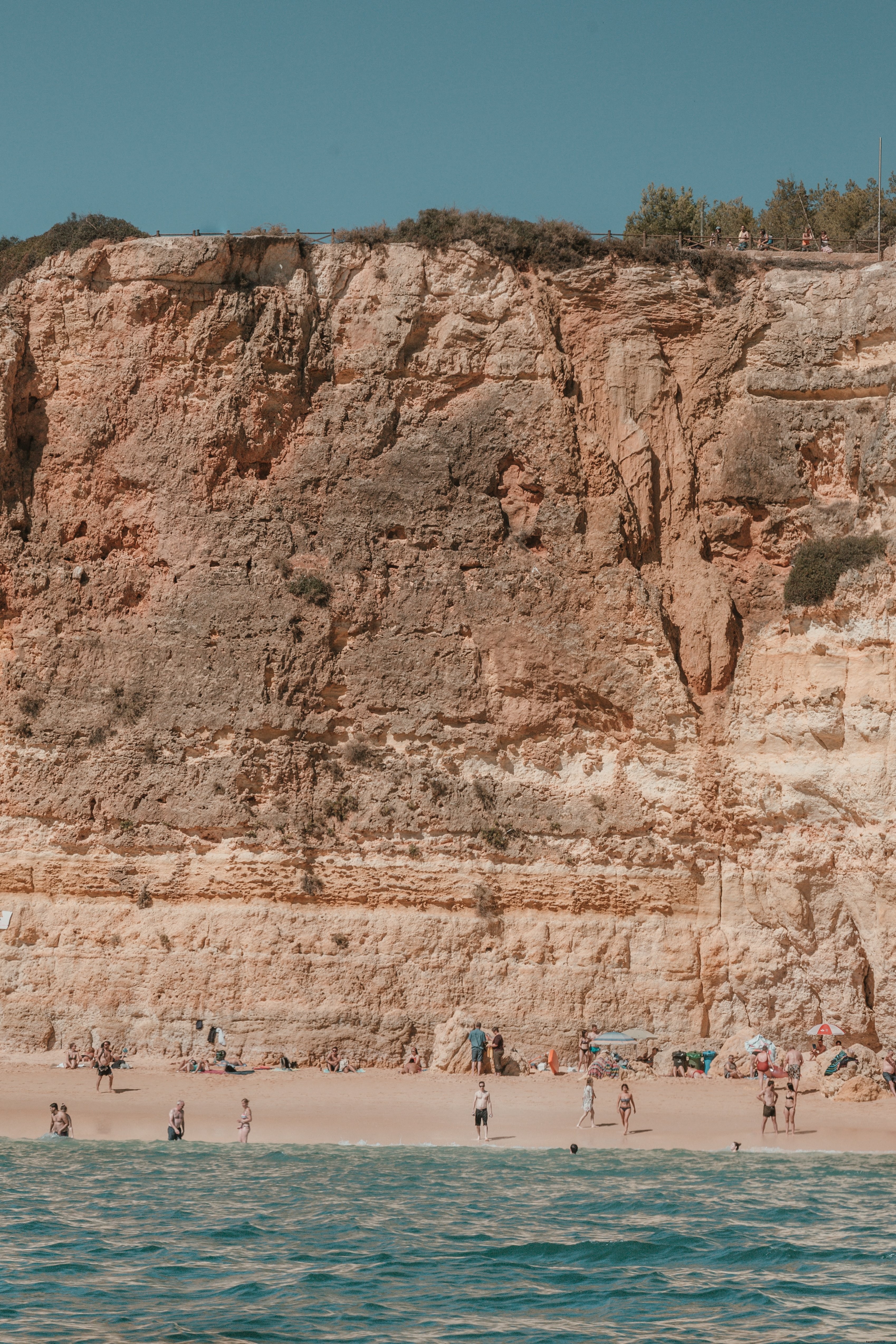 Scogliere spaccate dal sole si affacciano sui bagnanti su una spiaggia sabbiosa Photo