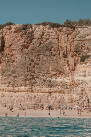 Penhascos rachados pelo sol com vista para banhistas em uma foto de uma praia de areia