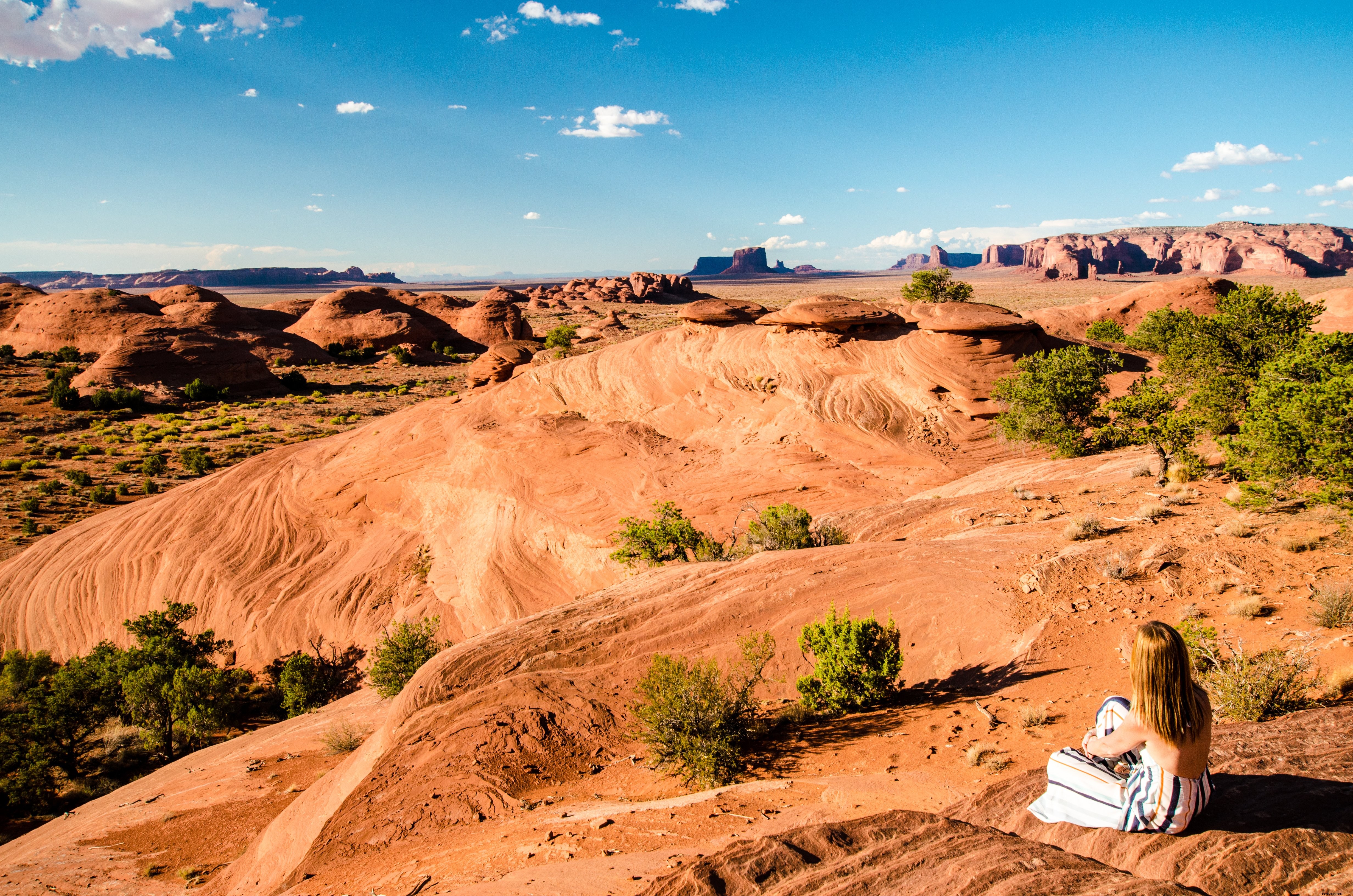 Foto de uma mulher sentada em uma colina no deserto com vista para as planícies montanhosas