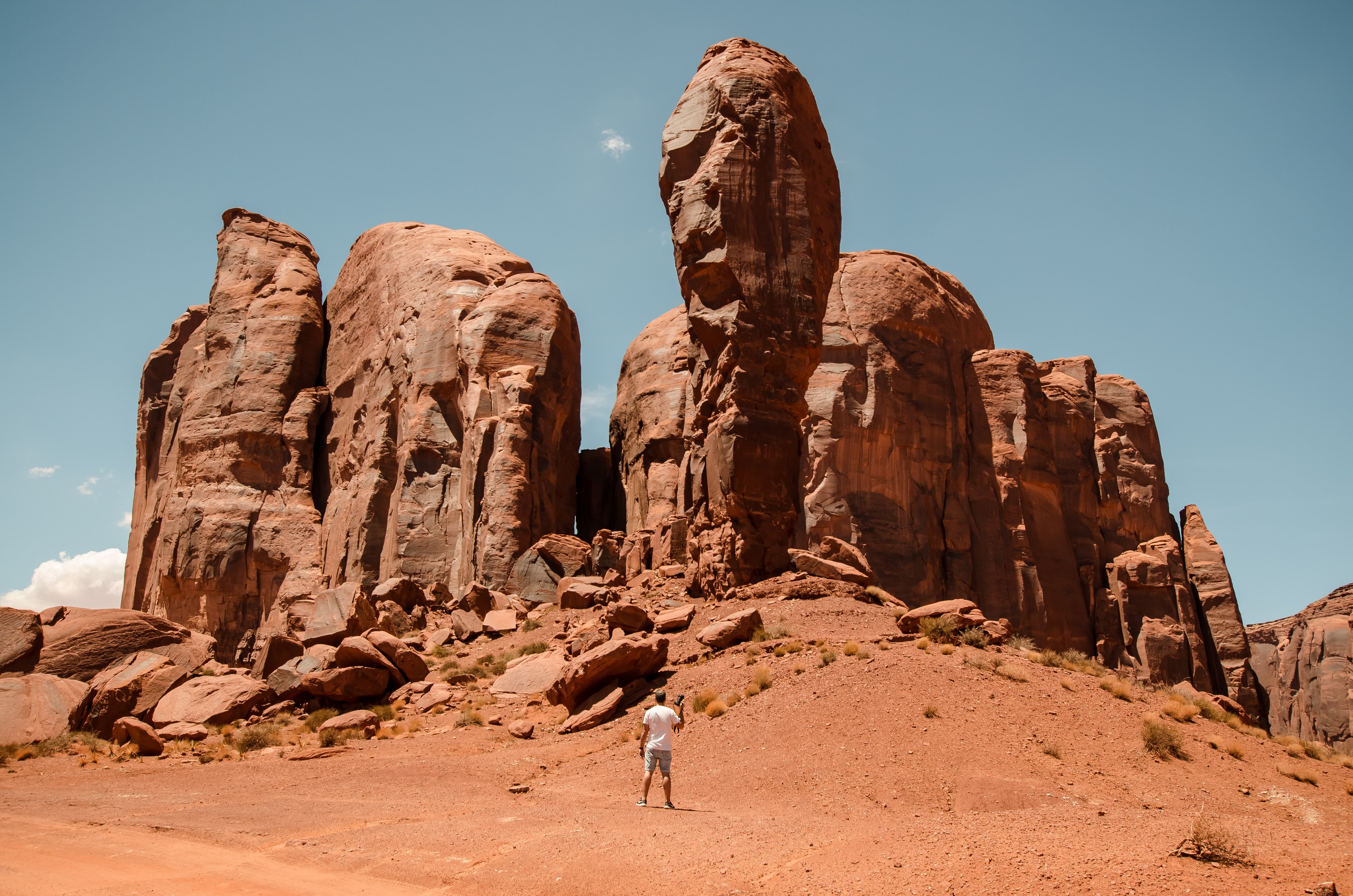 カメラを持った男が赤い砂漠の柱に向かって小さく立っている写真