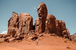 カメラを持った男が赤い砂漠の柱に向かって小さく立っている写真