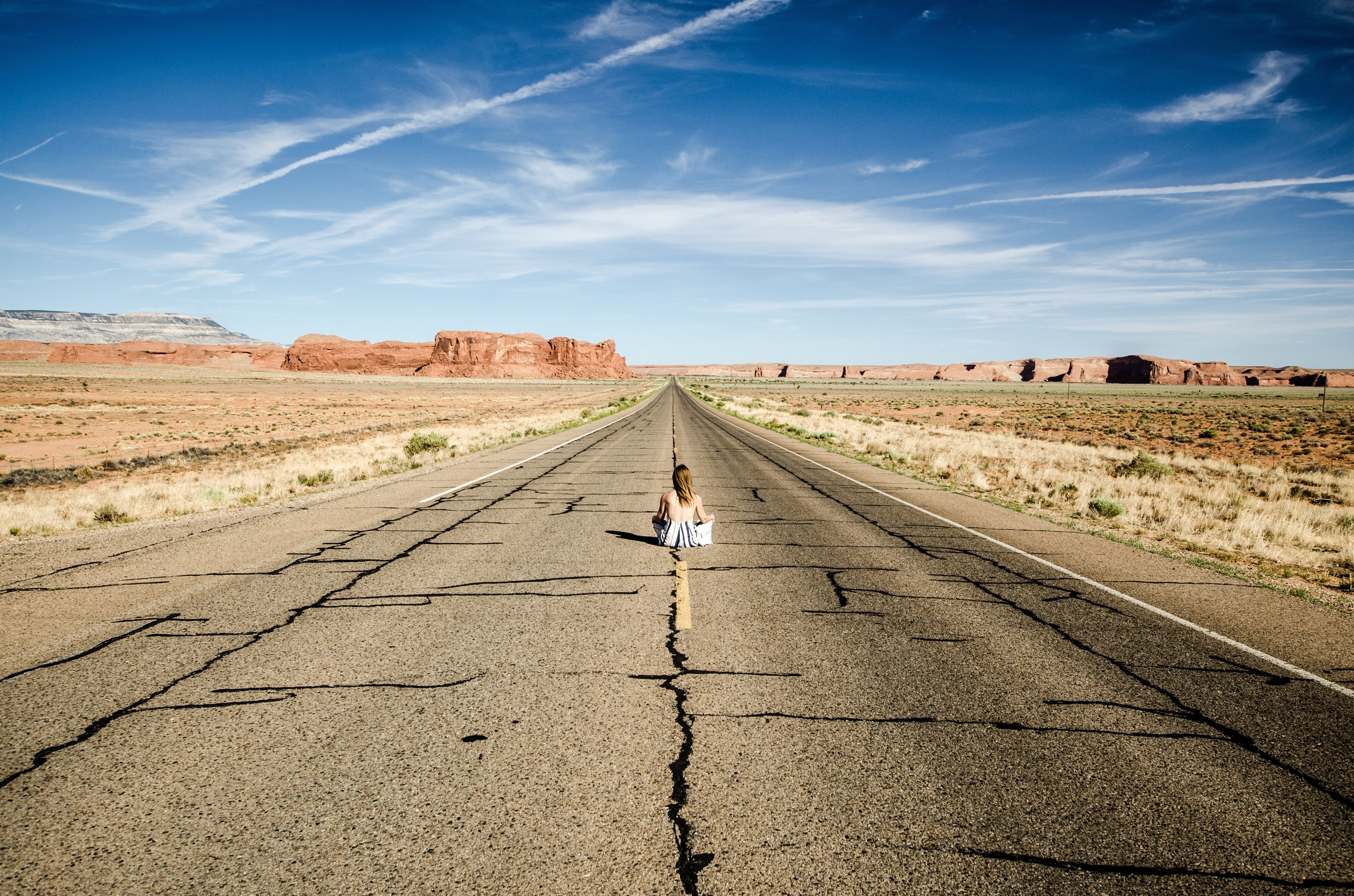 Foto de uma mulher sentada no meio de uma rodovia no deserto
