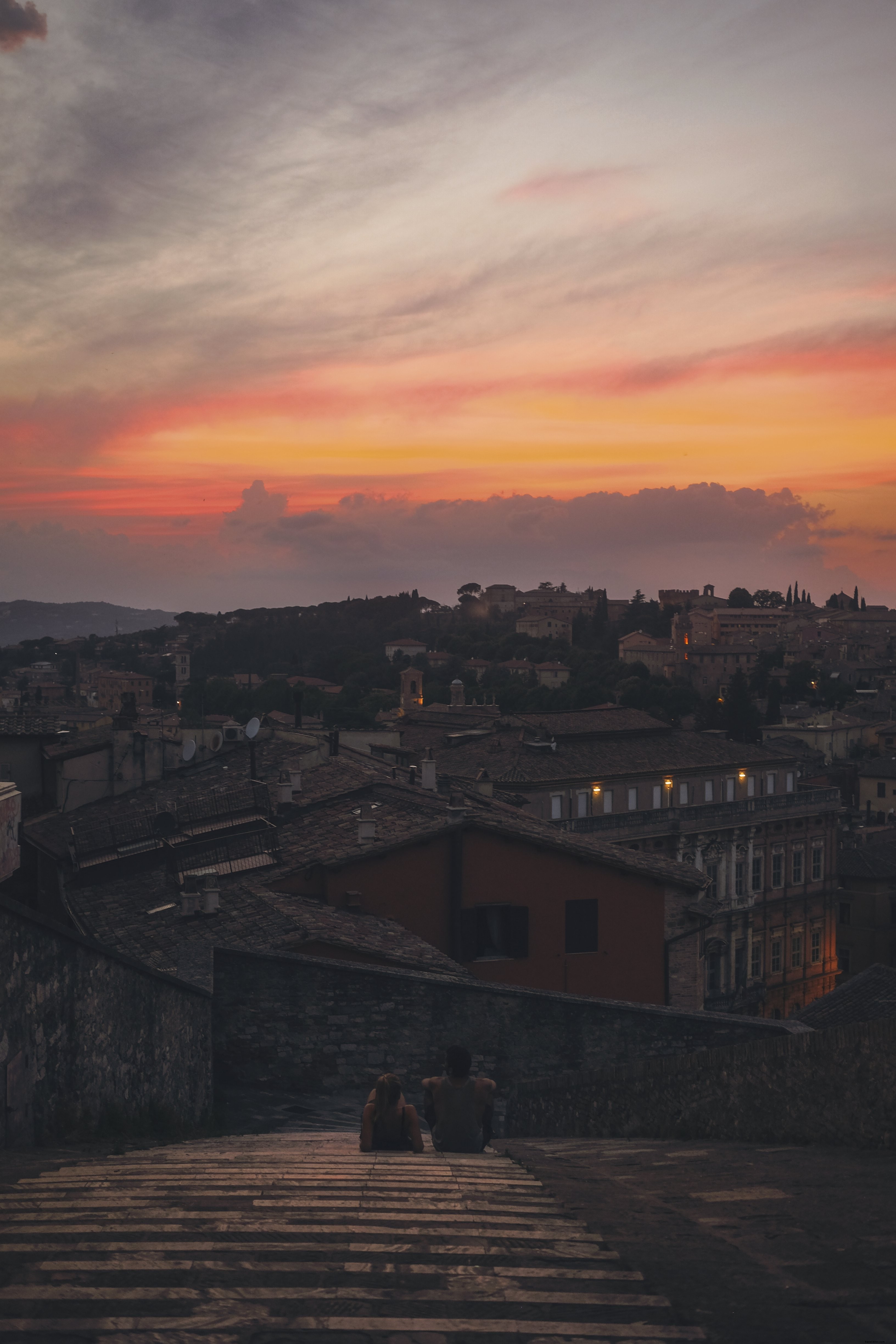 Duas pessoas sentam-se no alto para tirar uma foto do pôr do sol à noite