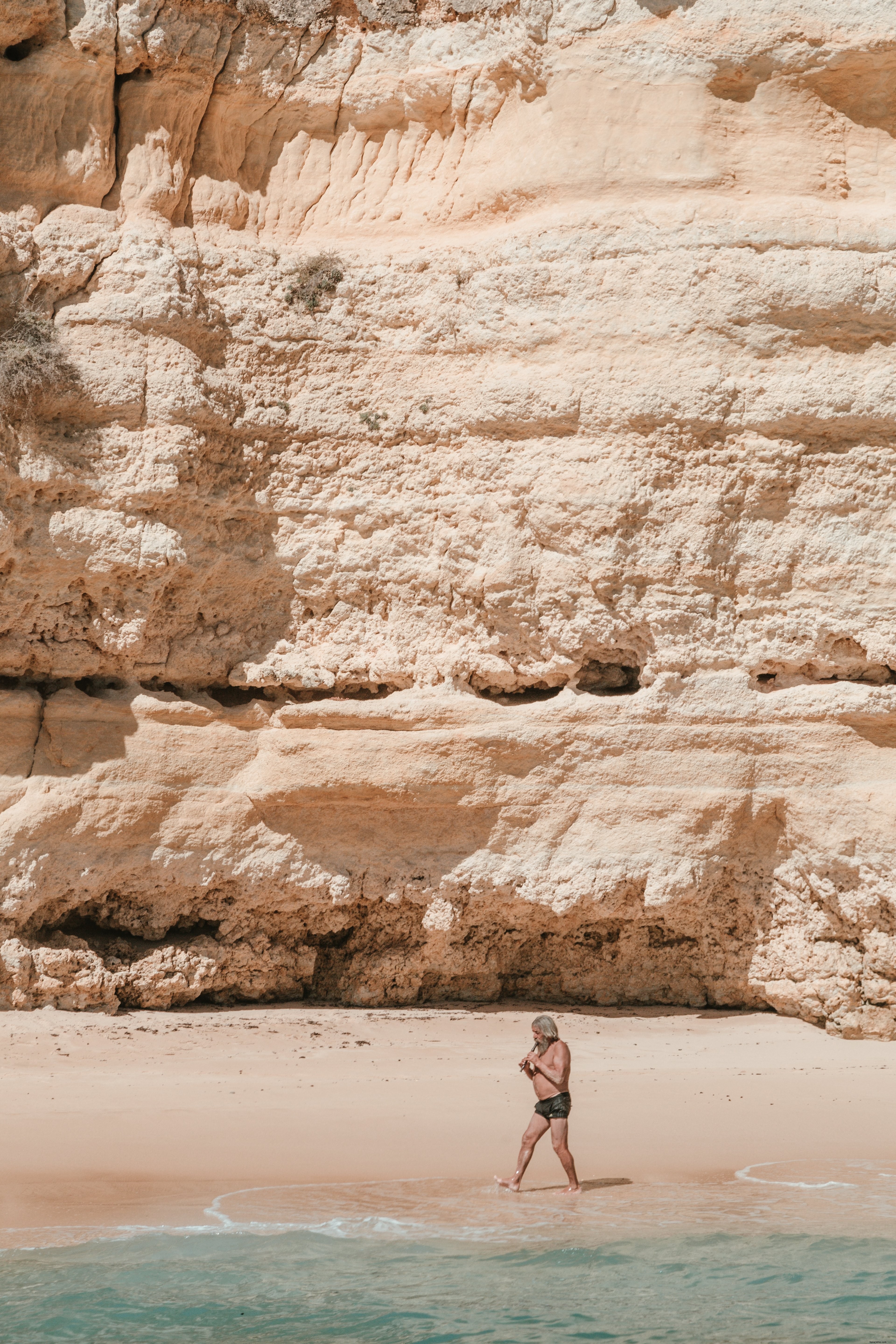 Un uomo anziano ingrigito suona la pipa passeggiando in riva al mare Foto