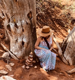 カウボーイハットの女性が砂漠の木のそばでしゃがむ写真