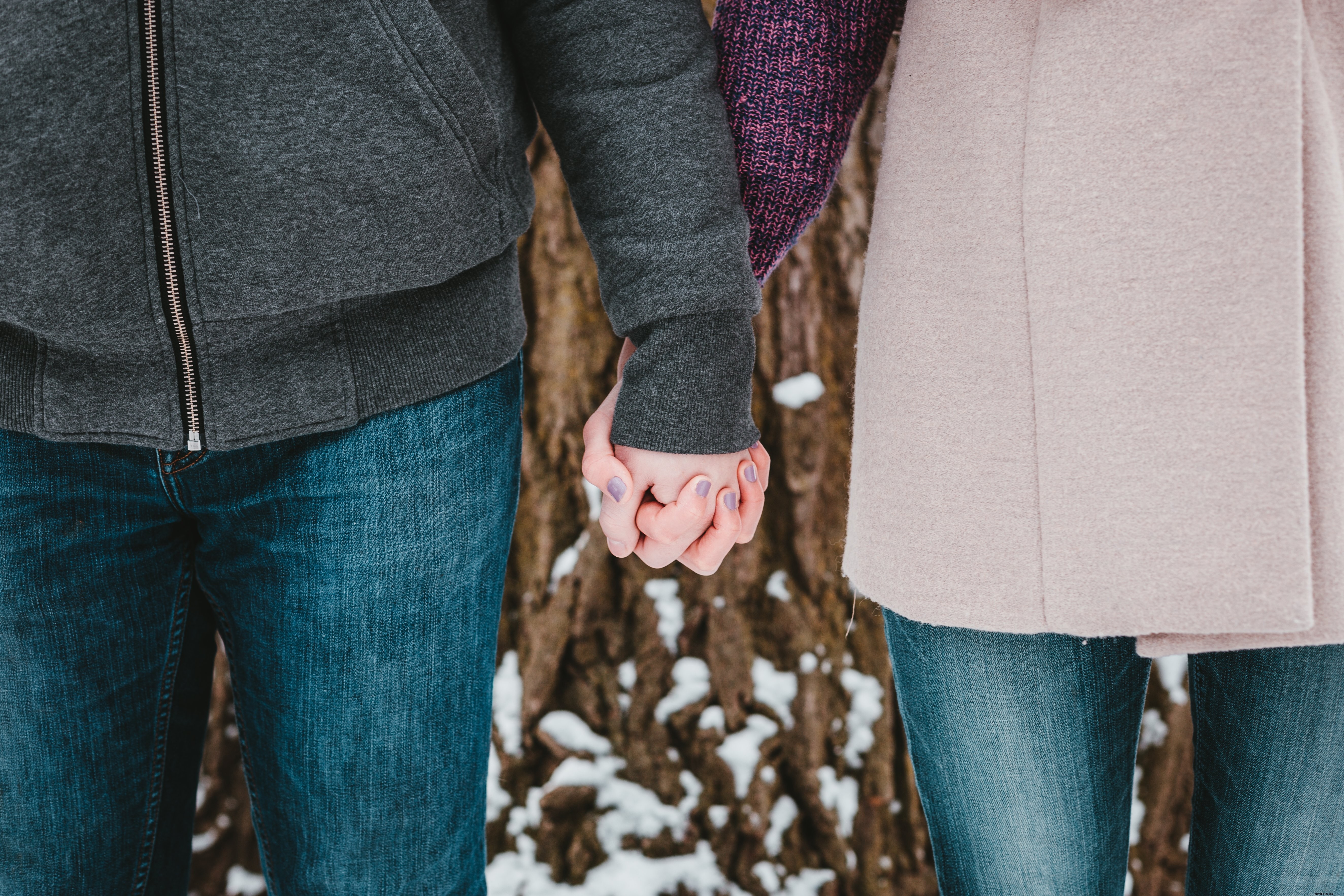 Foto de um casal de mãos dadas perto de uma árvore coberta de neve