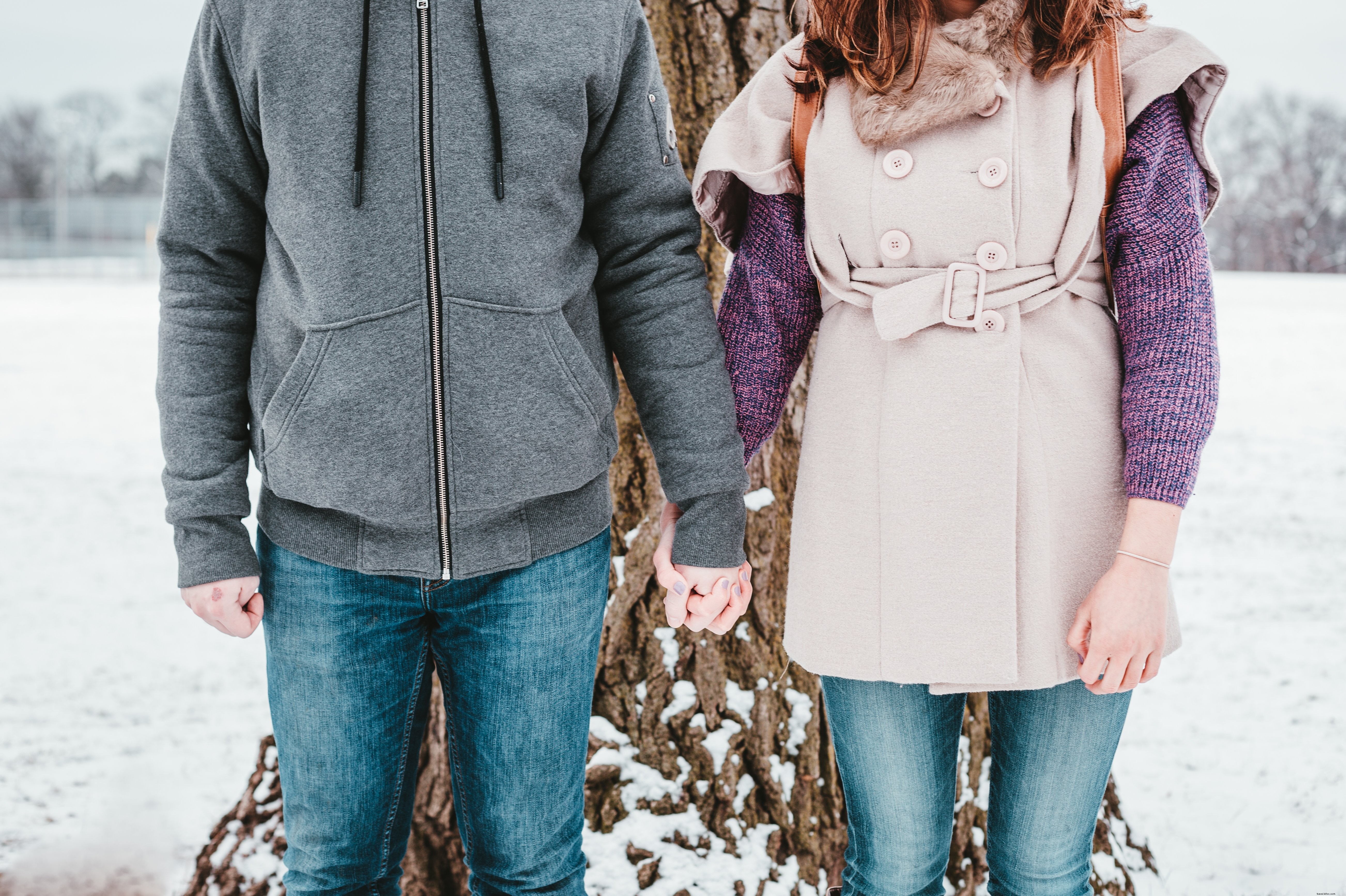 Um casal desafiando o inverno na frente de uma árvore alta.