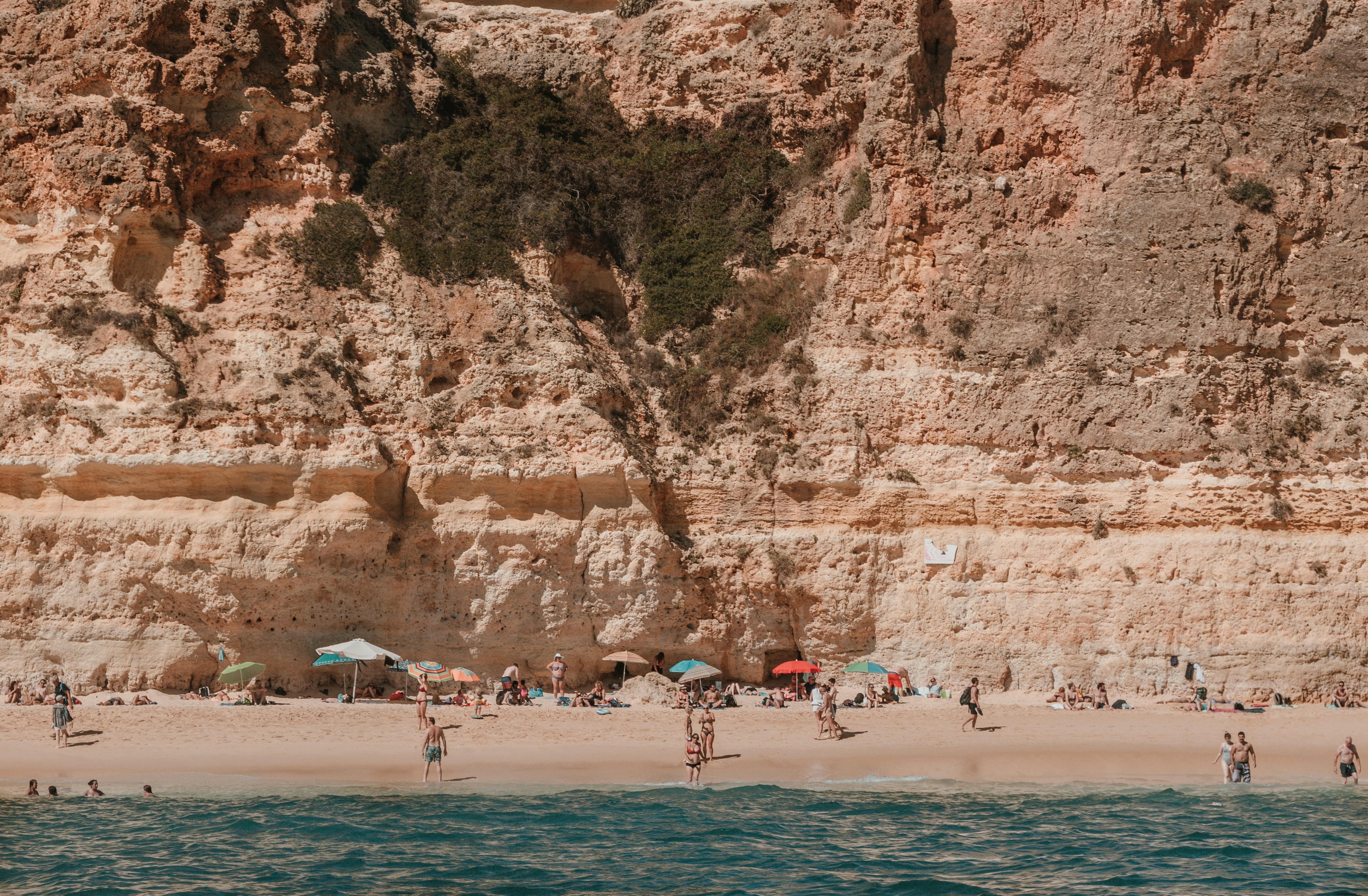 I bagnanti si crogiolano su una spiaggia assolata sotto le scogliere rocciose Photo