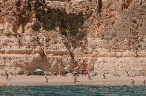 岩だらけの崖の下の日当たりの良いビーチで水着を浴びる写真