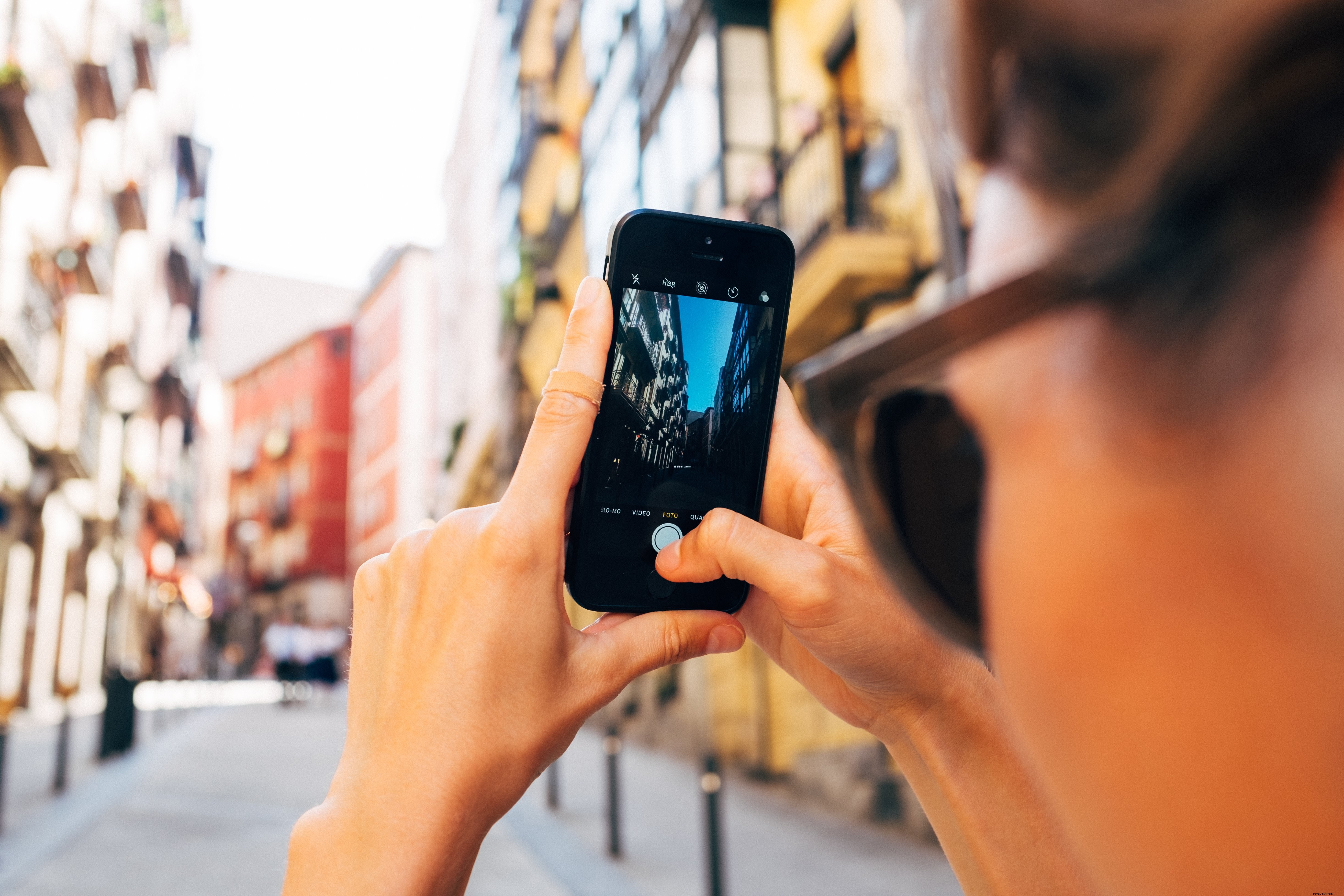 Uma mulher tira uma foto em seu celular em uma foto de rua ensolarada
