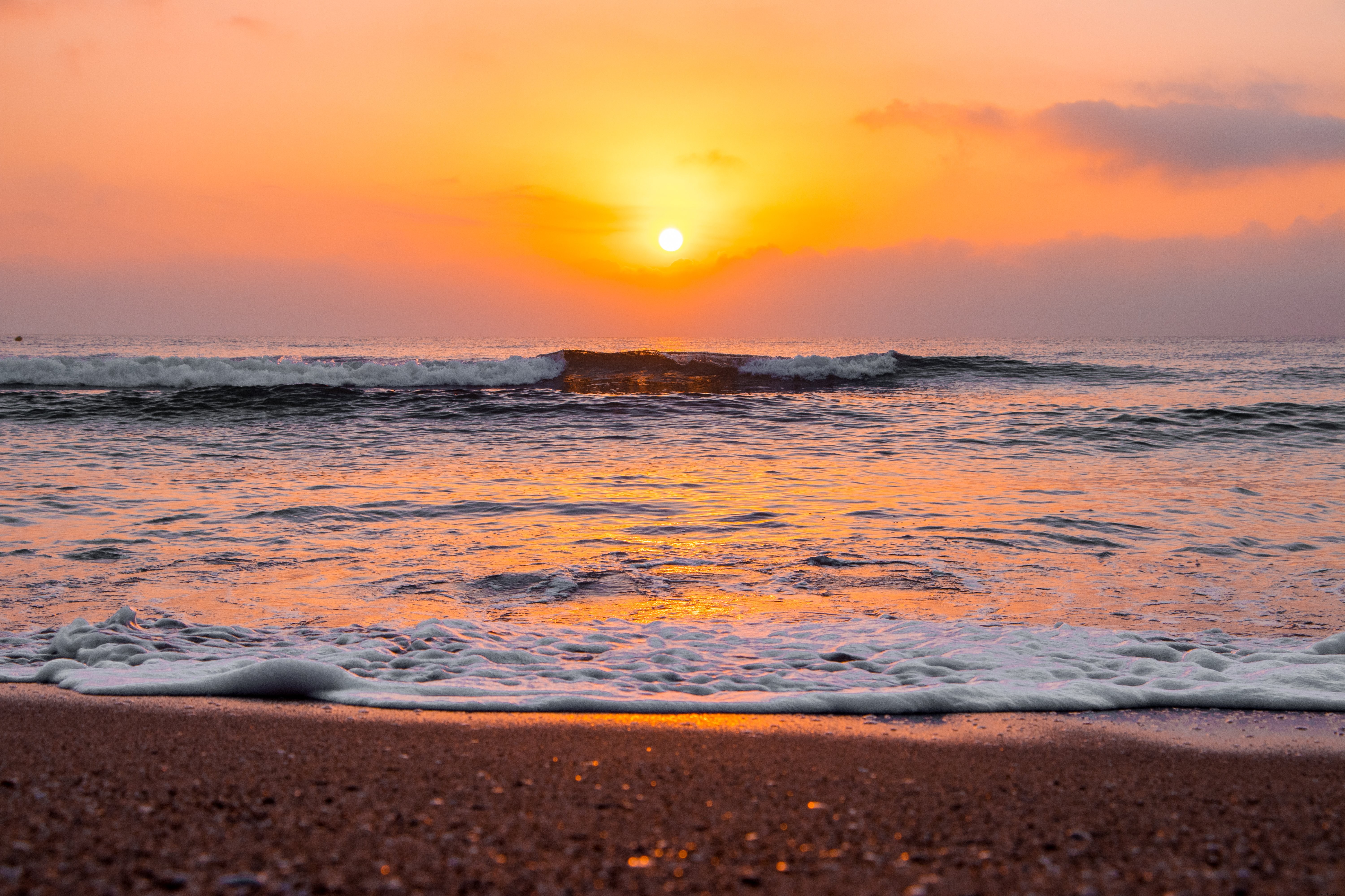 Foto do nascer do sol sobre o oceano ondulado na praia de areia