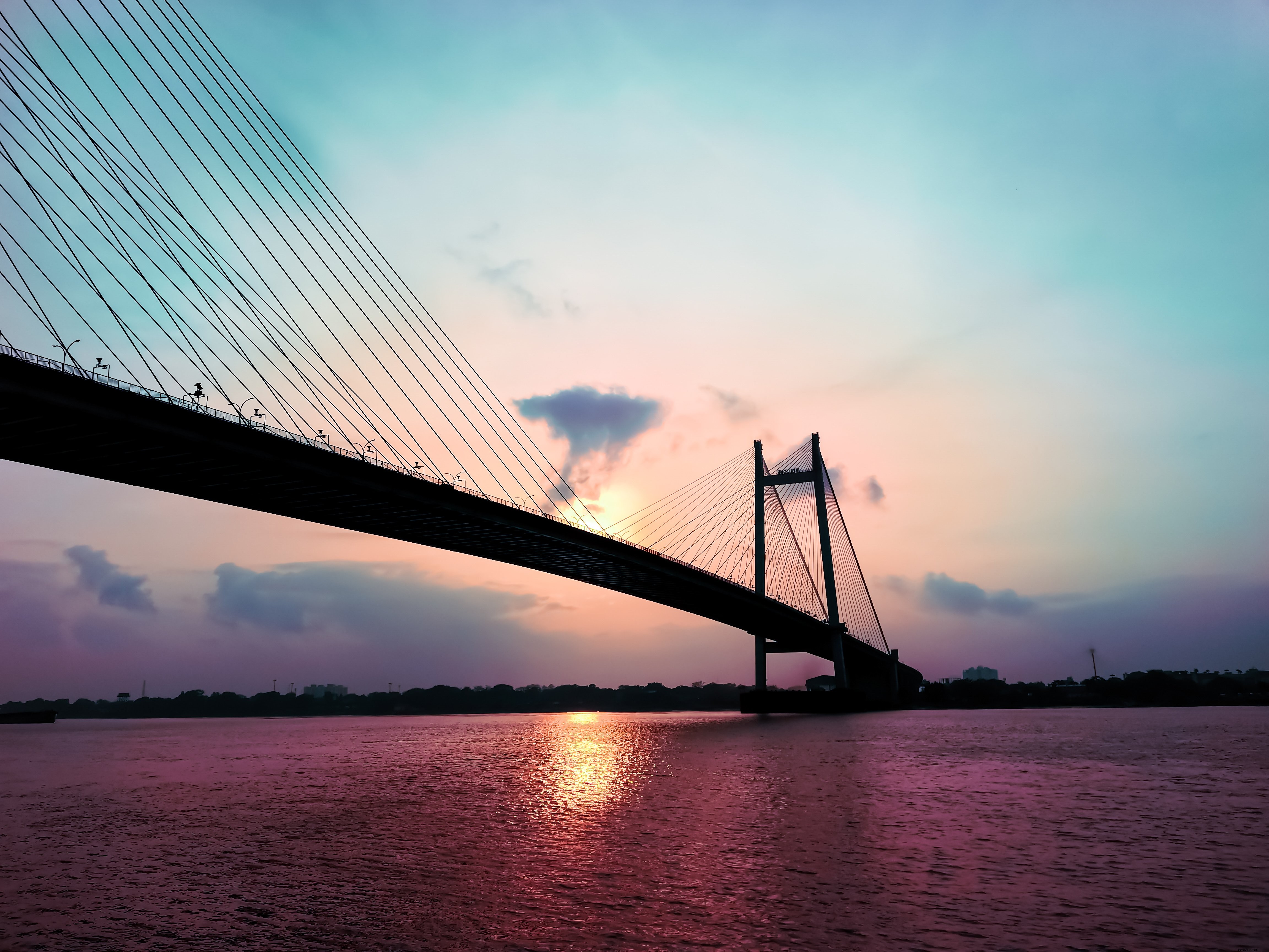 A silhueta de uma ponte suspensa pela foto do pôr do sol