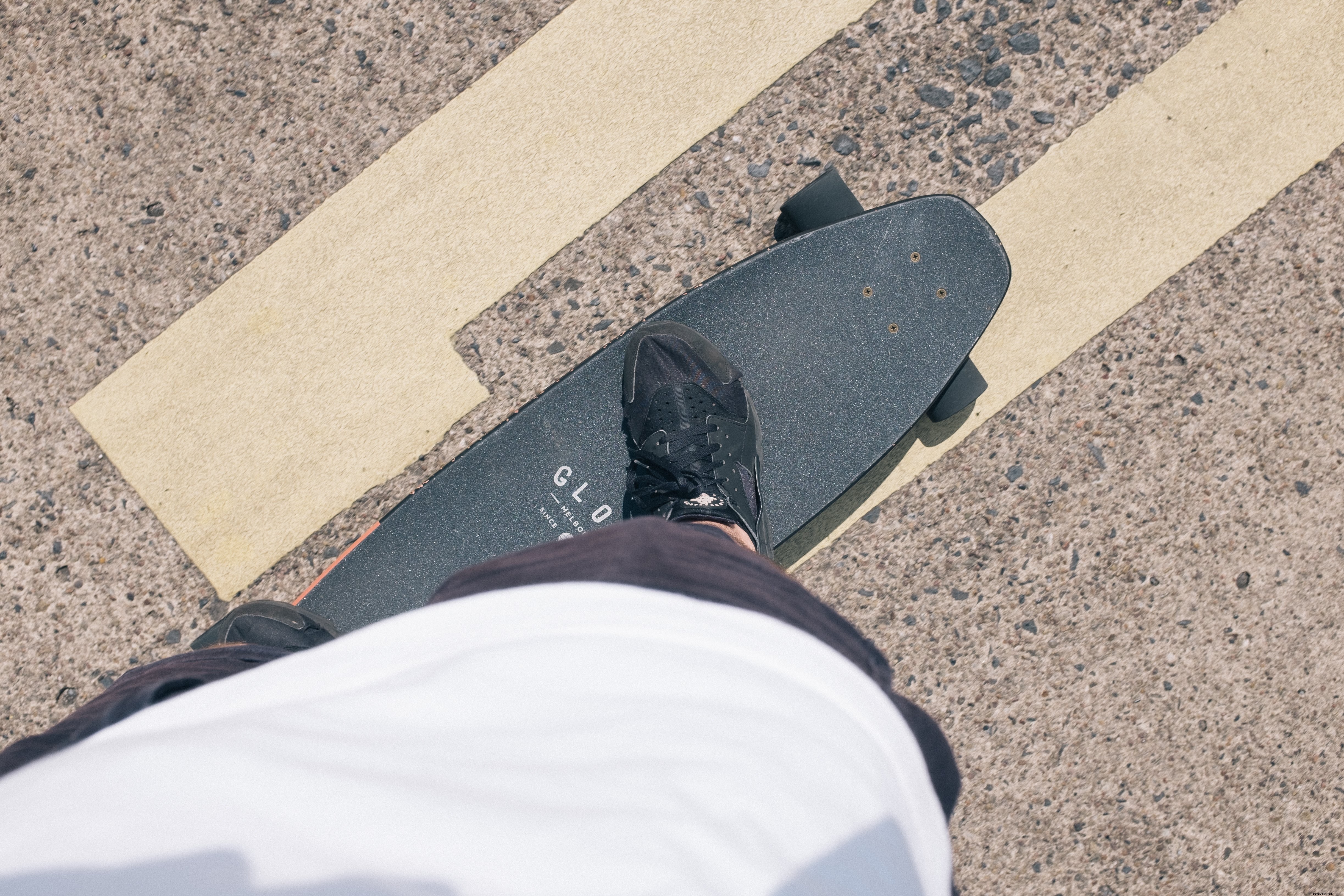 Foto de pessoa em pé em um skate preto em uma estrada pavimentada