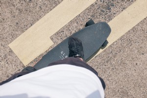 Foto de pessoa em pé em um skate preto em uma estrada pavimentada