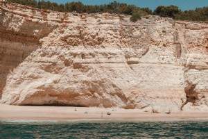 石灰岩の断崖の下の砂浜のカヤックとサーファーの写真
