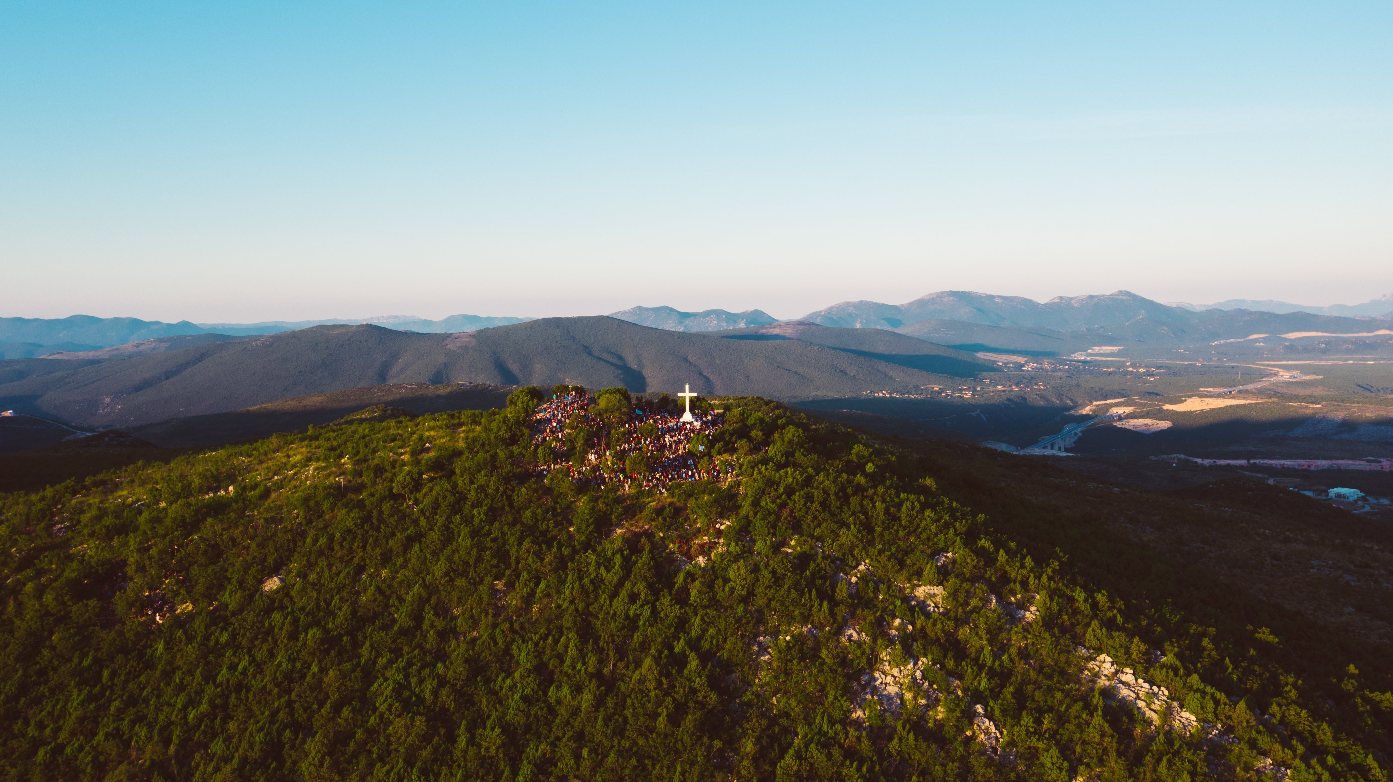 Turistas visitan una gran cruz parada en una foto de la cima de una montaña