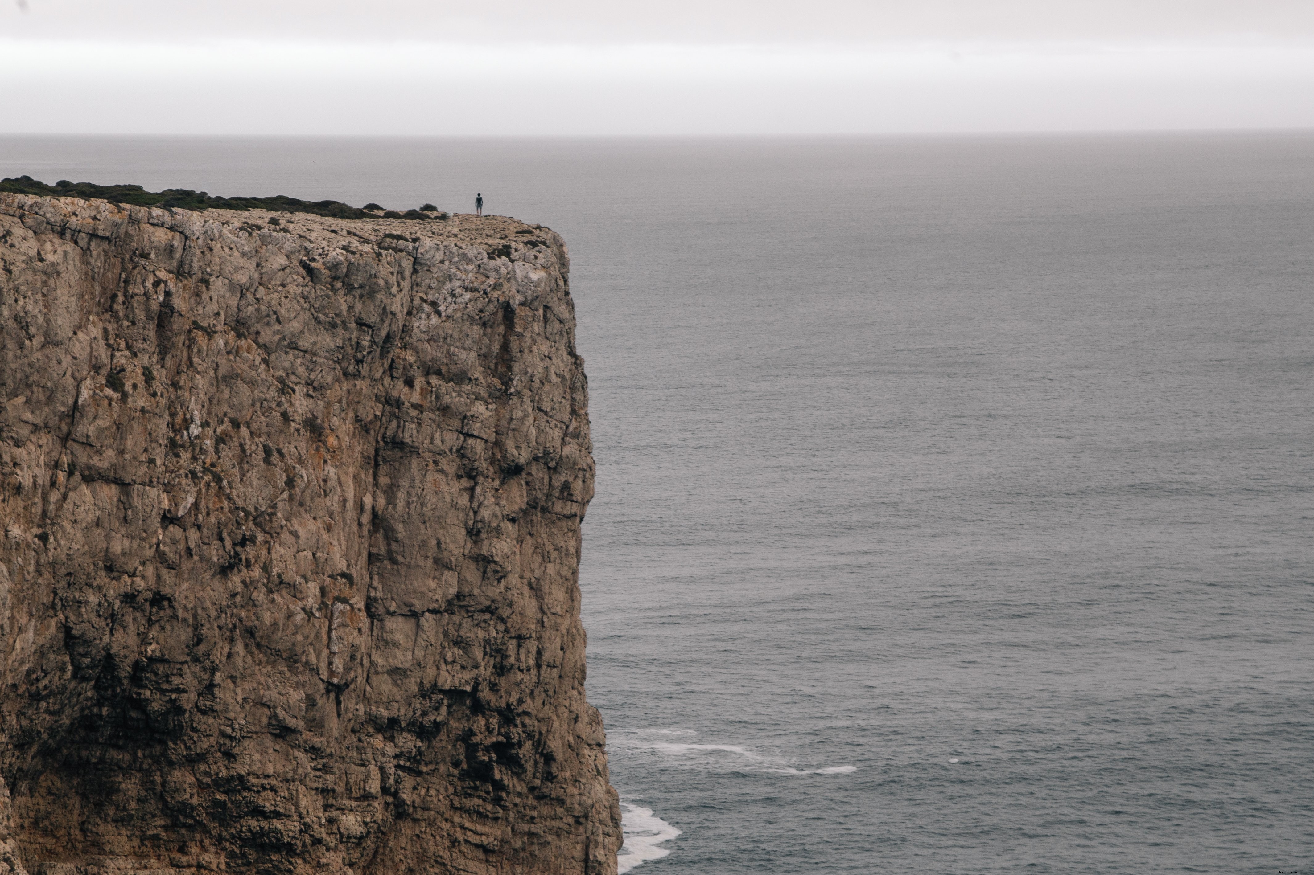 Una figura en un acantilado con vista al mar bajo un cielo gris Foto 