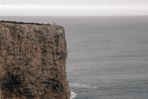 Una figura en un acantilado con vista al mar bajo un cielo gris Foto 