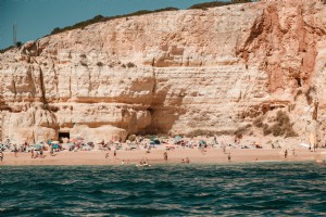 岩だらけの崖の写真に対して砂浜の入浴者 