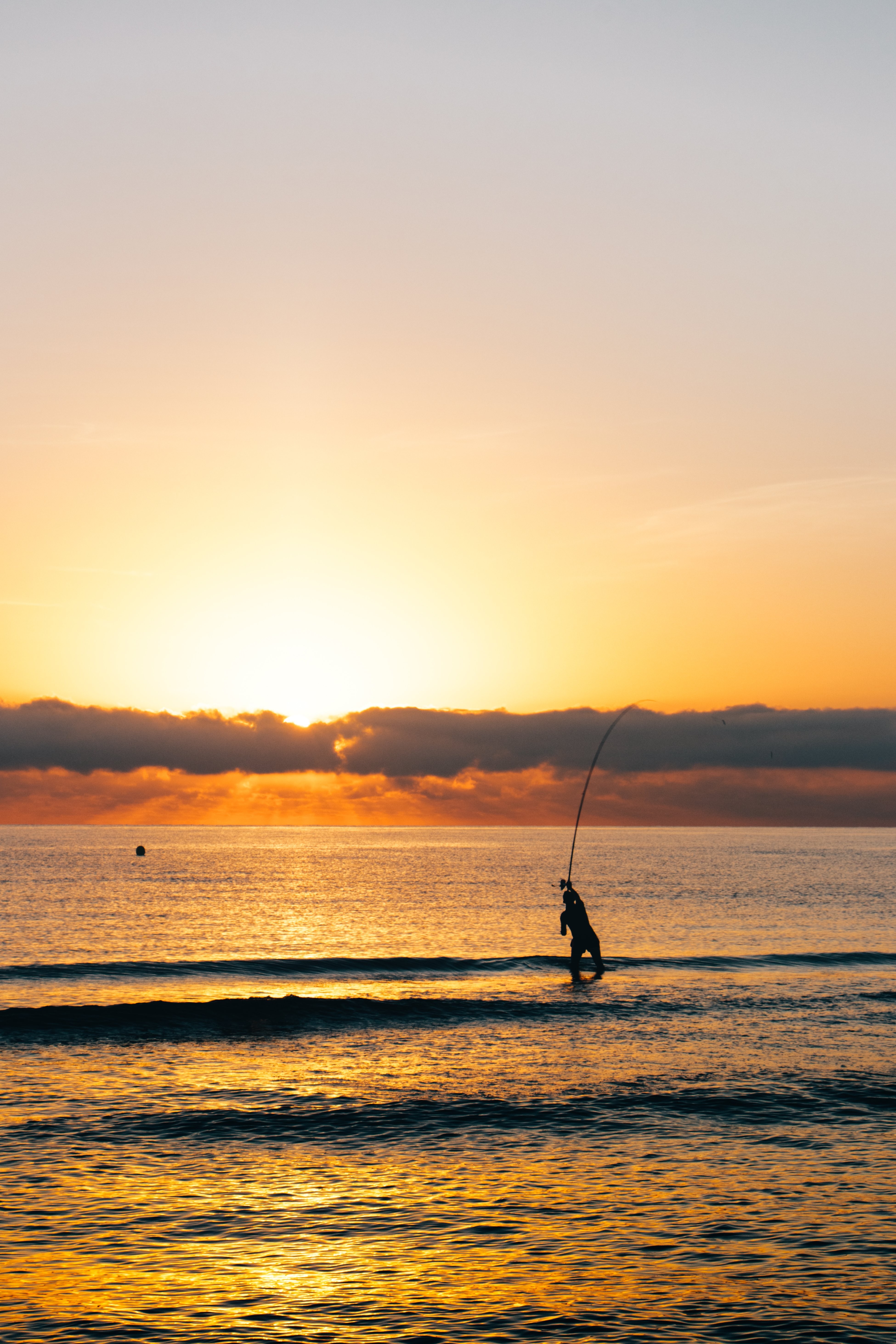 Pescador fica na água ao amanhecer. 