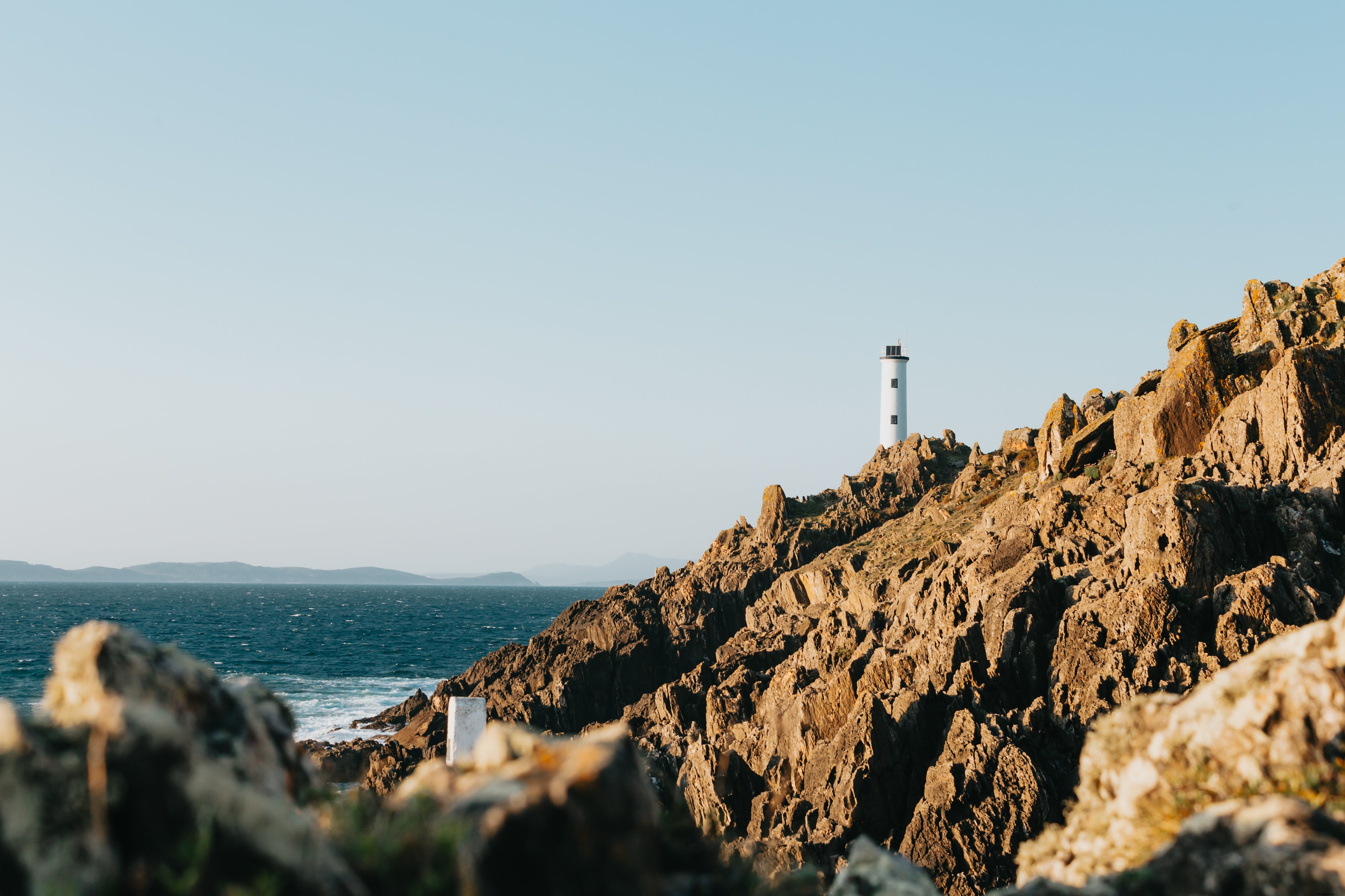 青い水の写真に対する鋭い岩の海岸線の背の高い灯台 